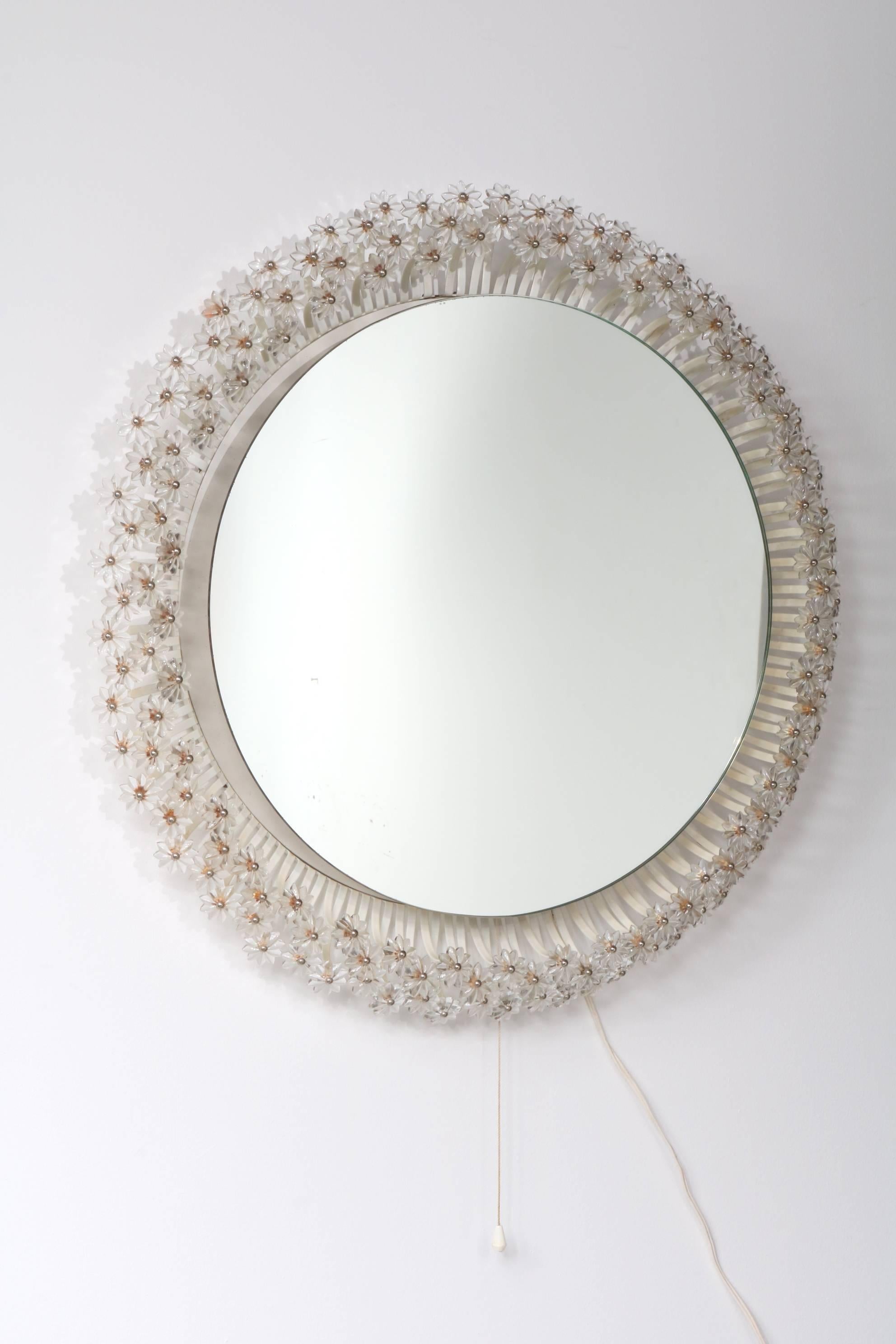 An outstanding backlit mirror designed by Emil Stejnar, manufactured by Rupert Nikoll in Austria around 1950.

The round mirror has an integrated frame with many beautiful little flowers made of glass with metal. This frame can be lit up, creating