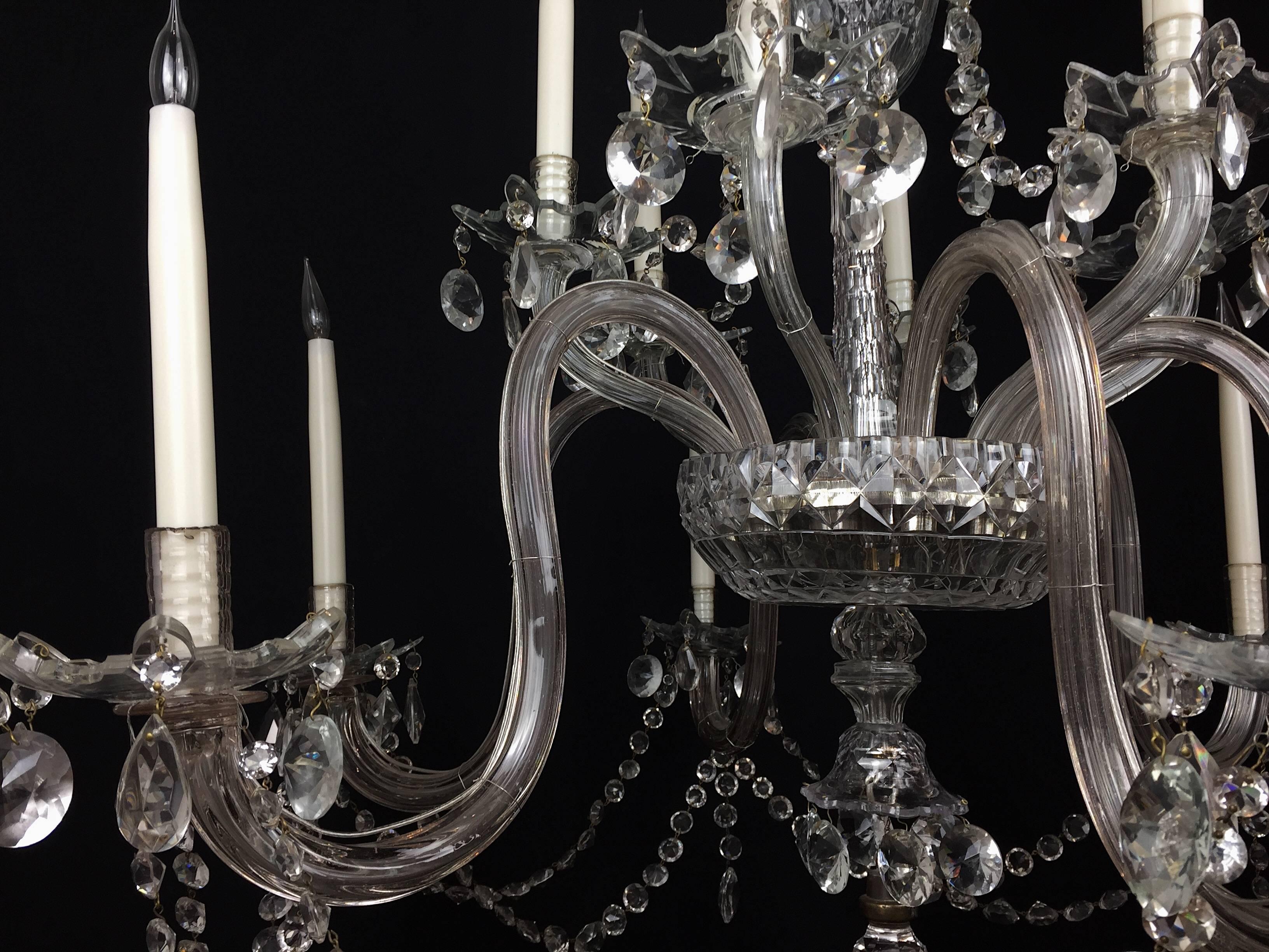 An English early 19th century six-arm chandelier in an 18th century style.

With a central ballista stem from which emulates six cut-glass S-shaped arms and six upward stretched arms which are profusely hung with hand cut diamond faceted buttons
