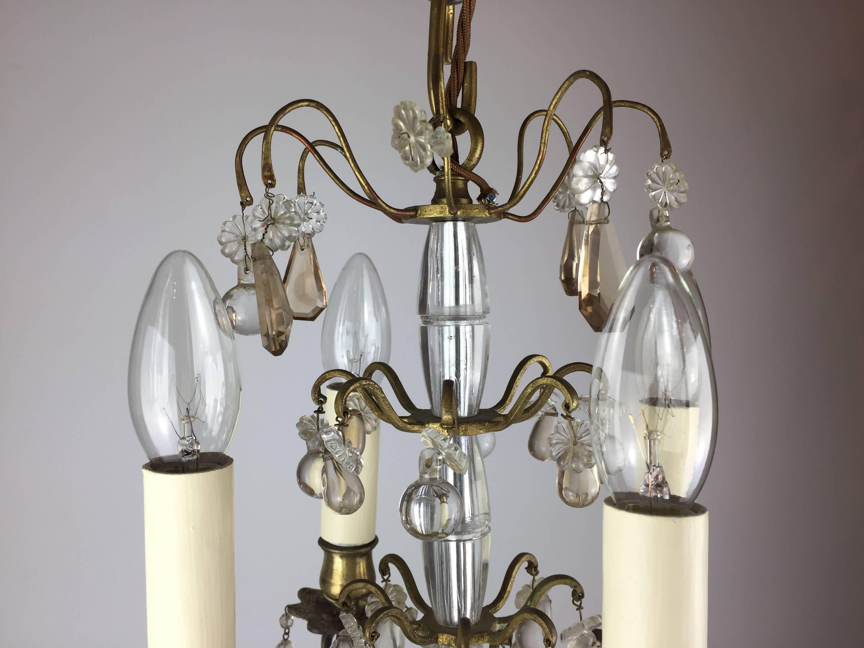 A small, gilt brass and cut-glass chandelier. Four arms of light, emulating from a glass column, hug with small clear and colored glass drops.