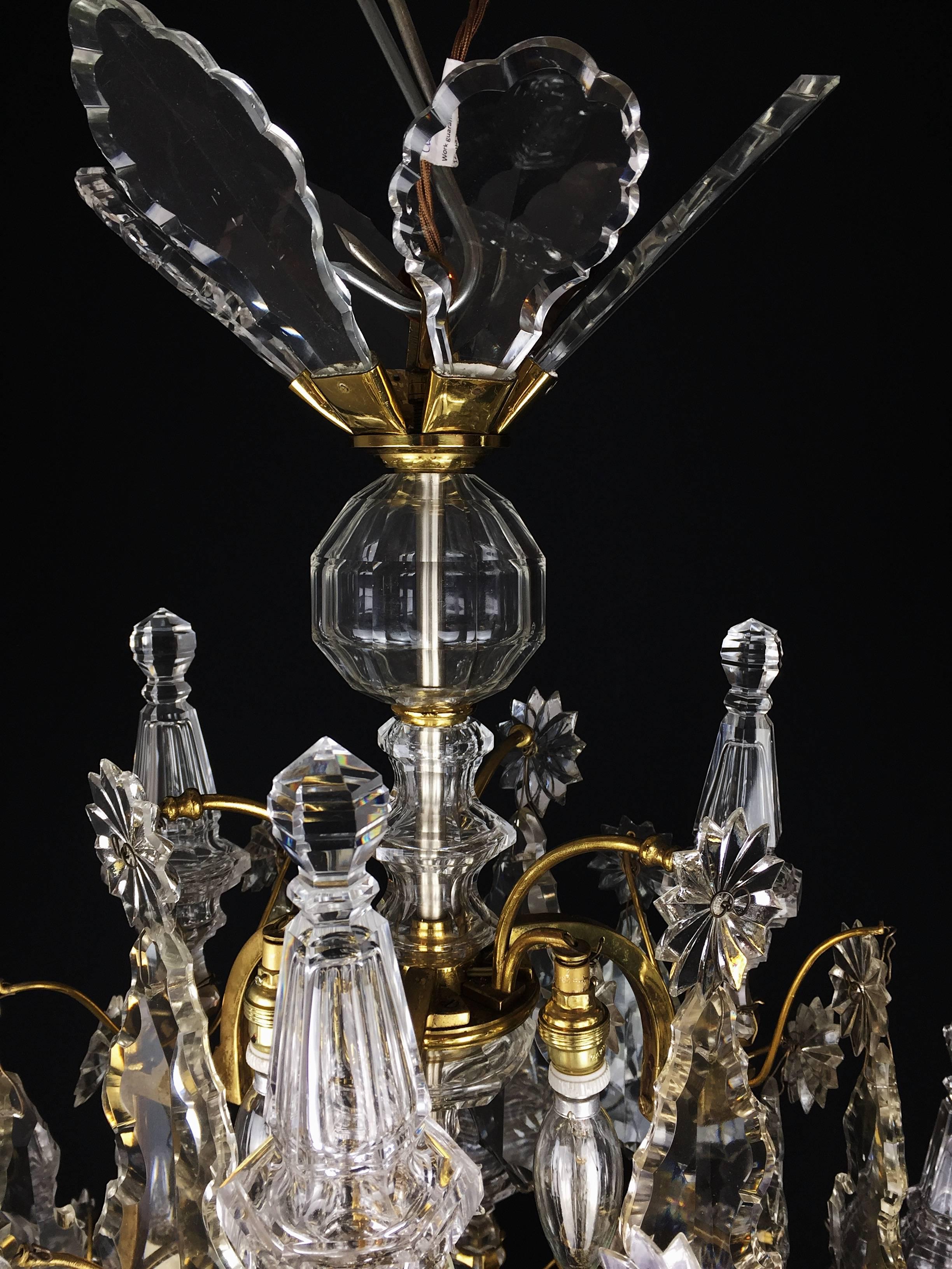 A large baccarat cut-crystal and ormolu chandelier with six curved arms of light decorated with drop-hung drip pans, slice-cut drops, and lower centrally lit pygmy lights. There is a rosette and an alternation of transparent and colored crystal