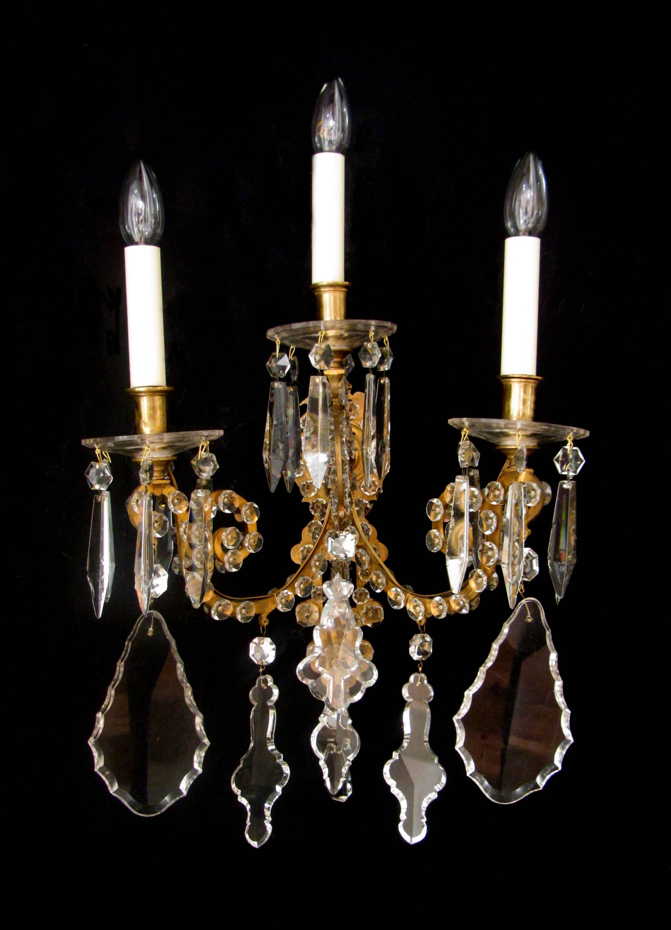 A large and elegant pair of gilt brass and crystal scrolling three arm wall lights, with large hand cut plaques, drip pans and crystal studs. 