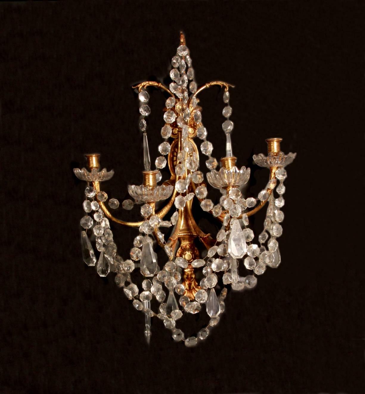 A pair of Louis XVI style gilt brass and crystal four arm wall lights. Profusely decorated with swags of crystal buttons, faceted, icicle and albert drops, with pretty cut-glass dishes, French, late 19th century. Can be professionally wired for