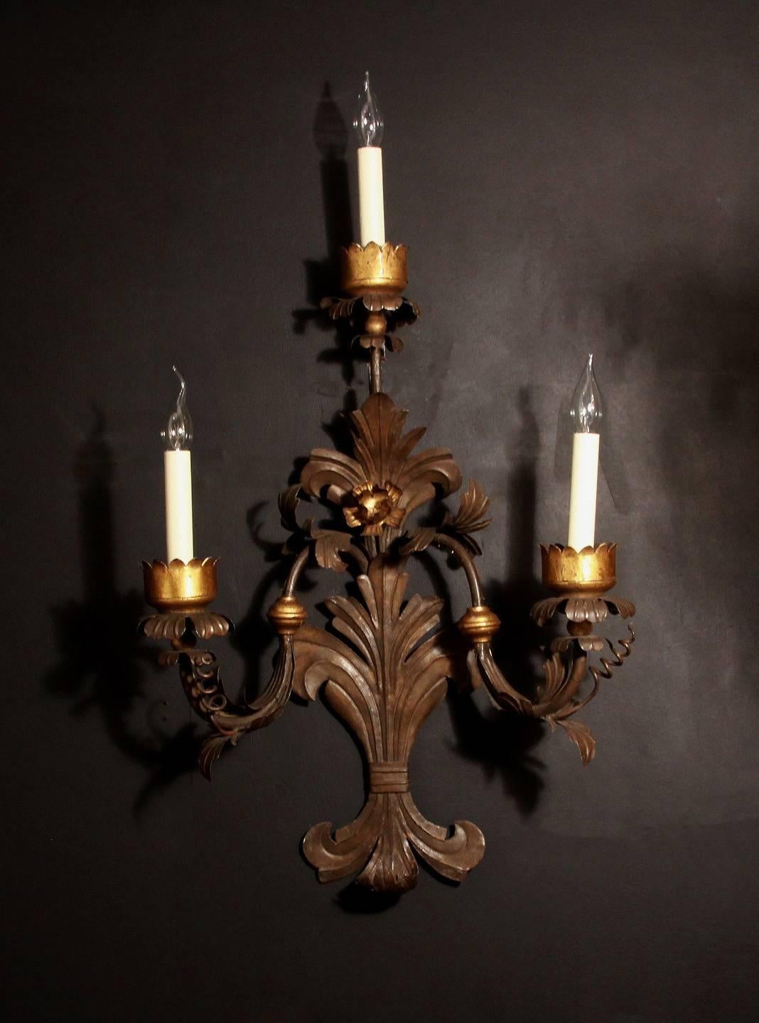 A large pair of three light, metal tole scrolling wall lights. With outward swept arms in the 17th century style, with gold leaf decoration applied.