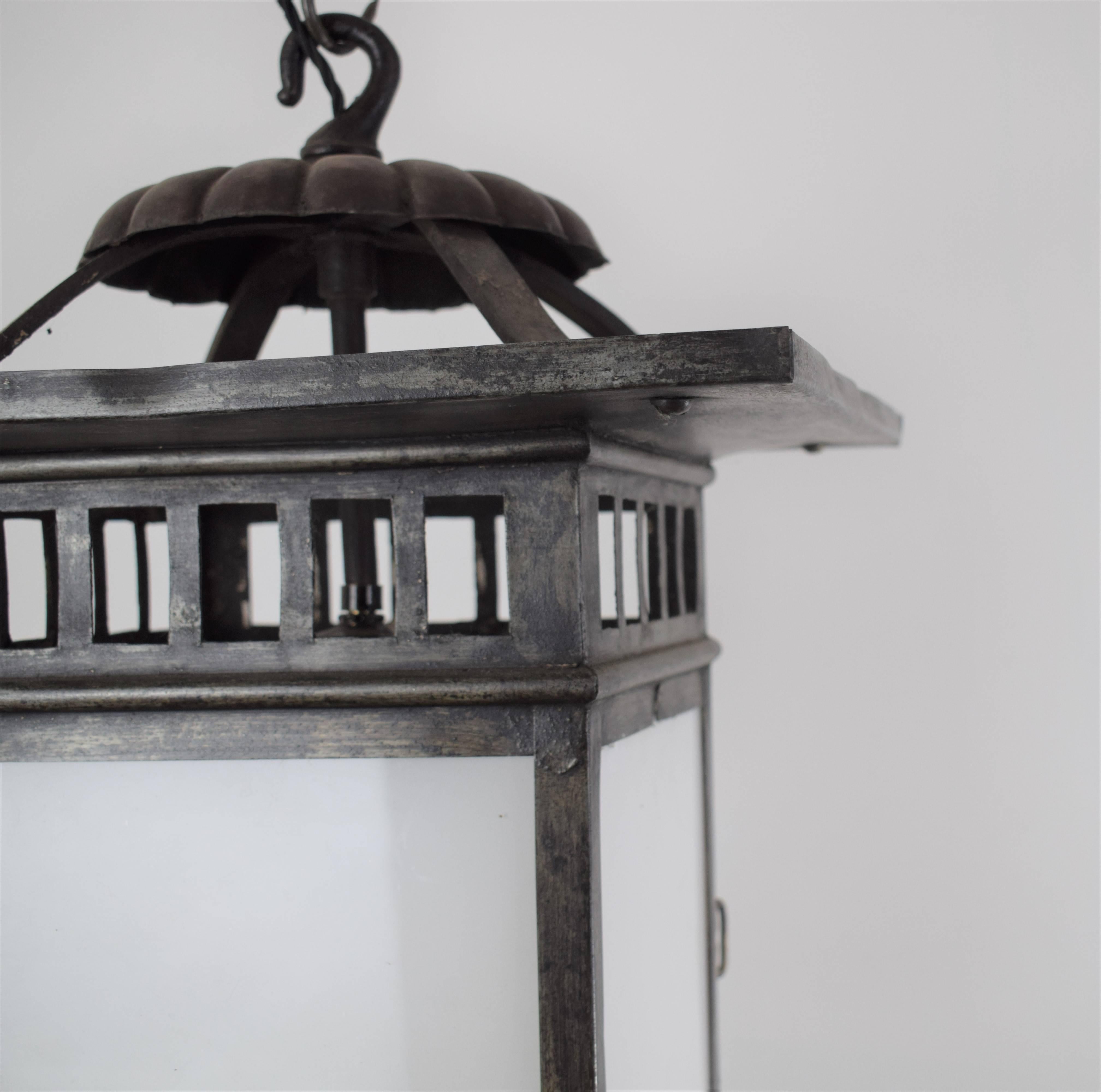 A fine arts and crafts metal lantern, with a puter and bronze finish. There is a single central bulb which is encased in panels of frosted glass. The four panels have a roof overlapping the lantern in the style of CFA Voysey, English, 1910.