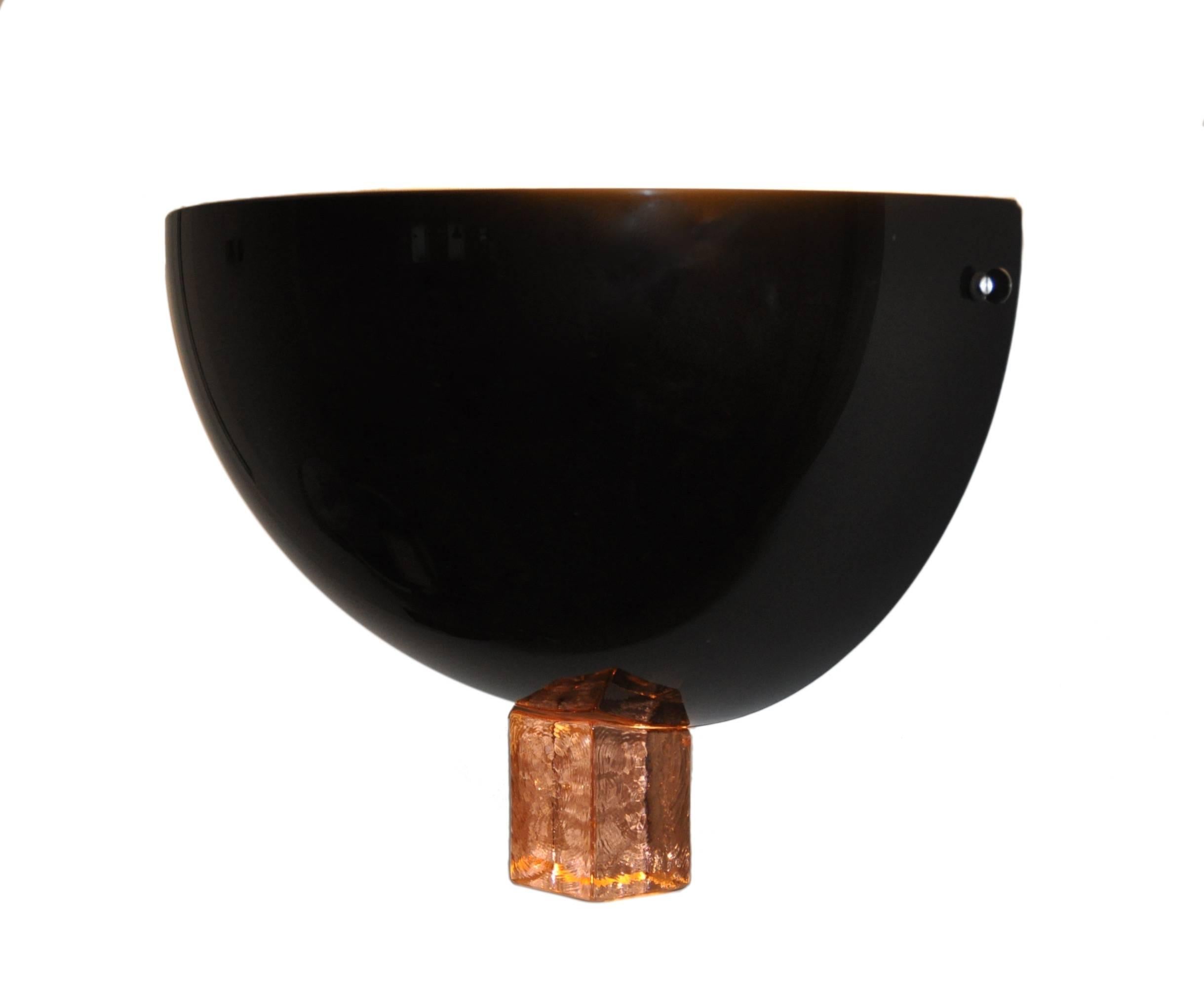 The appliques presented here were produced in two sizes this edition the biggest of the two, measuring an impressive 15.3/4″ width in black opaque glass. When the lamp is lit the light reflects across the supporting wall and through the orange
