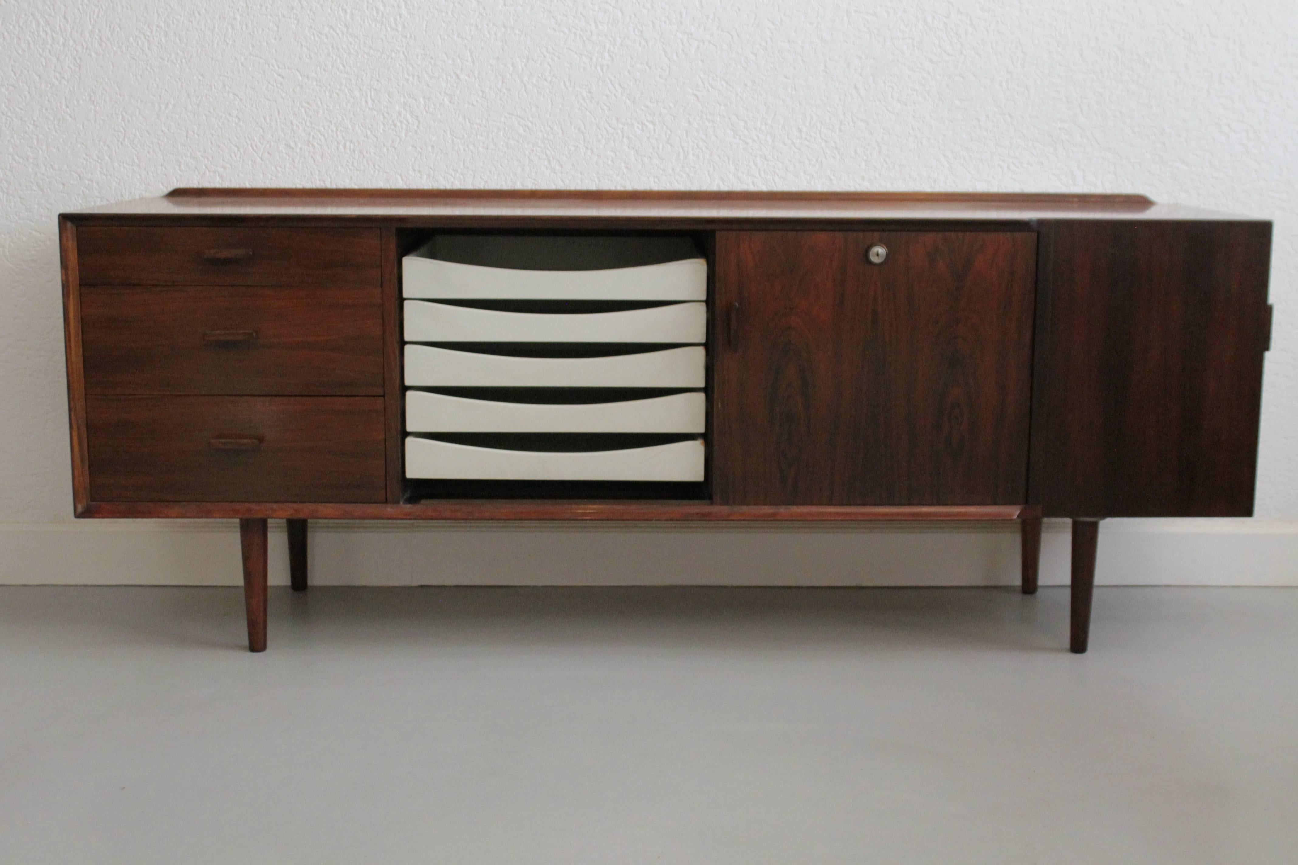 Arne Vodder rosewood sideboard with five white drawers inside
Three front drawers, one sliding and one side door.
Beautiful details
No keys
A hole as been done at the bottom of the side cabinet by the previous owner.
Produced by Sibast,