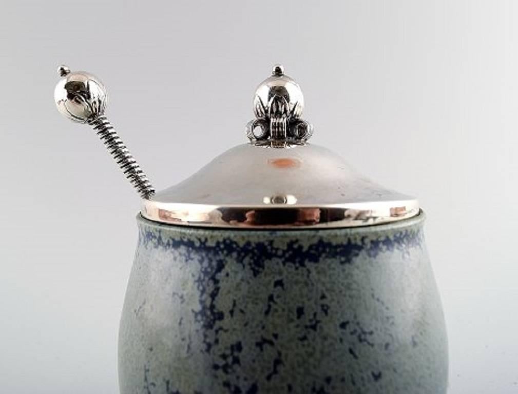 Arne Bang and others: b. Frederiksberg 1901, d. Fensmark, 1983.

Jam jar in stoneware decorated with speckled blue-green glaze. 

Lid and spoon in sterling silver.
Measures:
Height 13.5 cm.

Marked.

Casper, three towers silver,