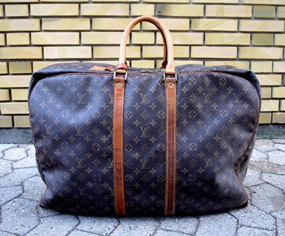 Louis Vuitton: An "Alize" travel bag of monogram canvas with two handles of leather, leather trimmings and a detachable name tag of bright cowhide leather, brass hardware and one large zip compartment with internal elastic straps.
