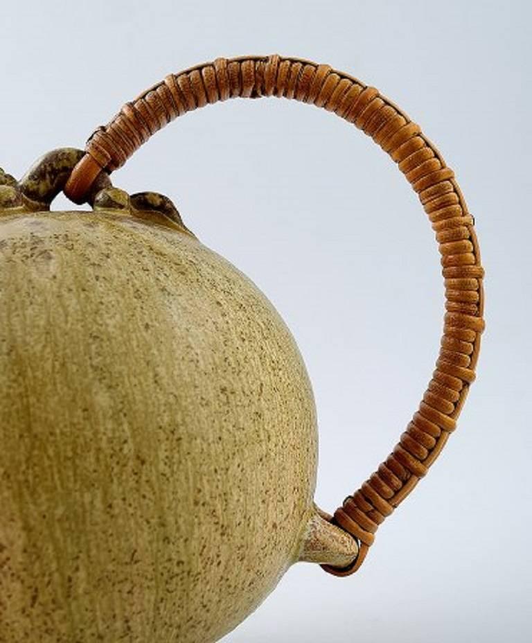 Arne Bang art pottery pitcher with wicker handle. 
Model number 151. 
Marked AB 151, Denmark, 1940s. 
Glaze in greenish shades.
 In perfect condition. Measures: 19 x 14 cm.
