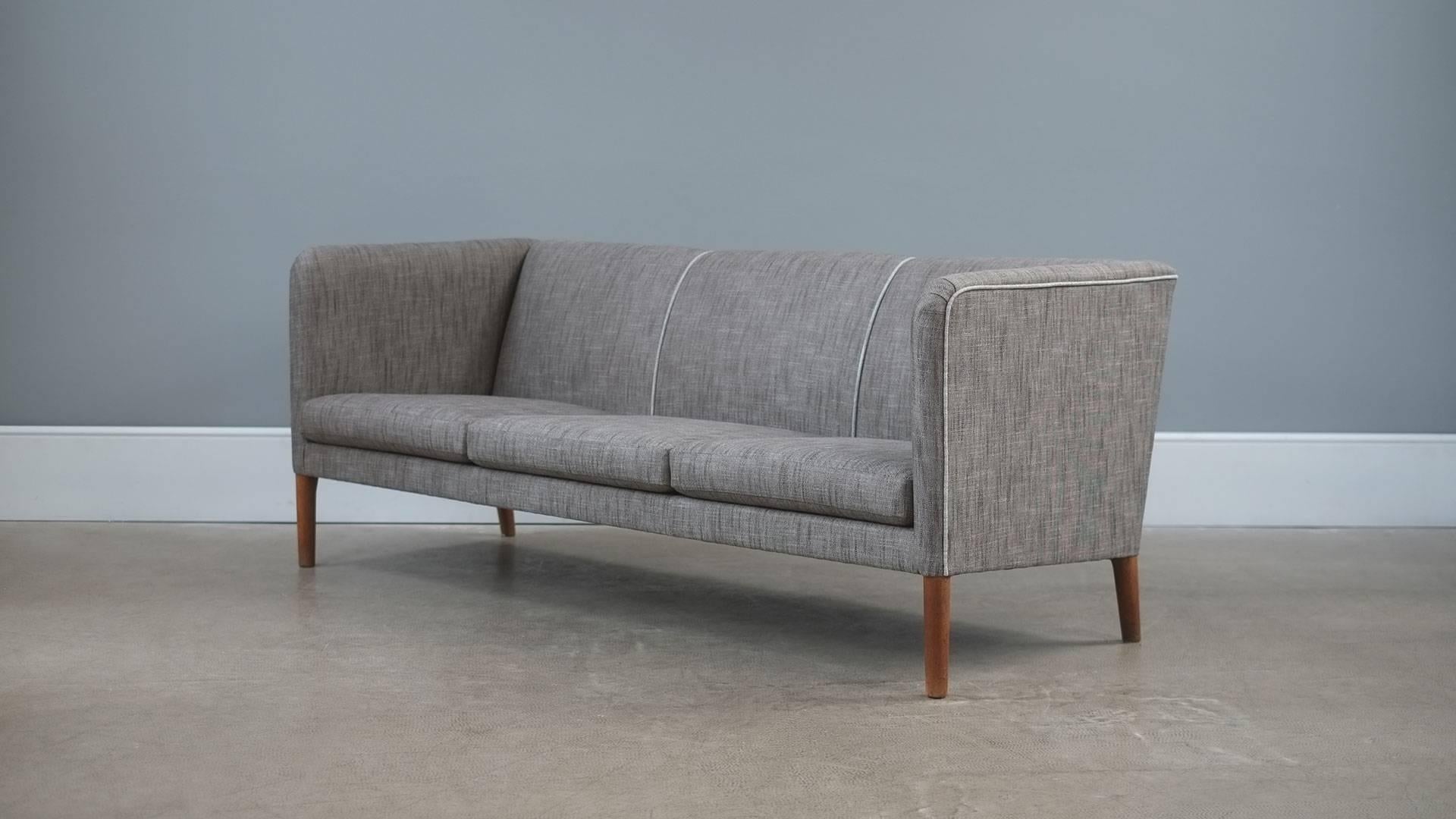 Ultra elegant Even Arm sofa designed by Hans Wegner for cabinet maker AP Stolen, Denmark. Very comfortable sofa fully reconditioned and reupholstered in fabulous grey fabric with contrasting piping details. Great piece.
 