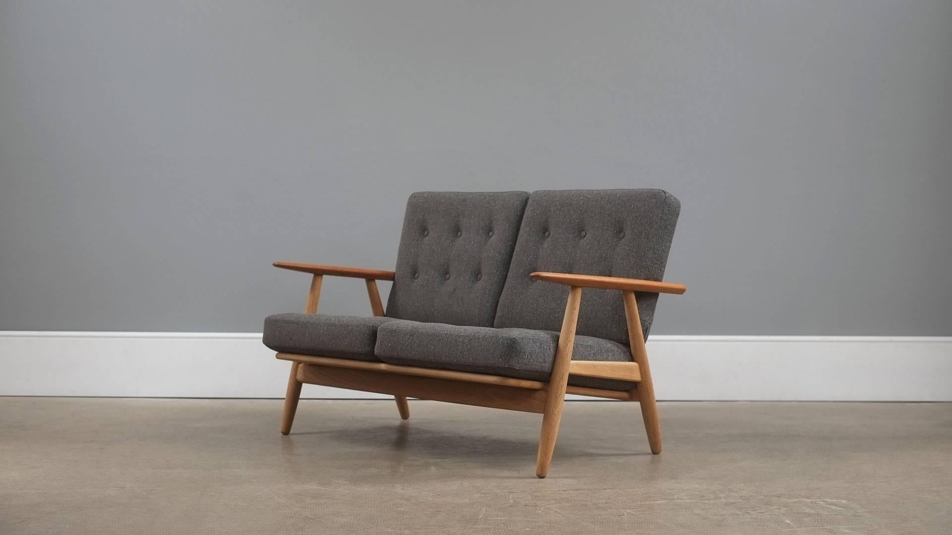 Beautiful GE240 two seat Cigar sofa in solid oak with contrasting teak arms designed by Hans Wegner for Getama, Denmark. Refurbished original sprung cushions with beautiful new fleck upholstery. 