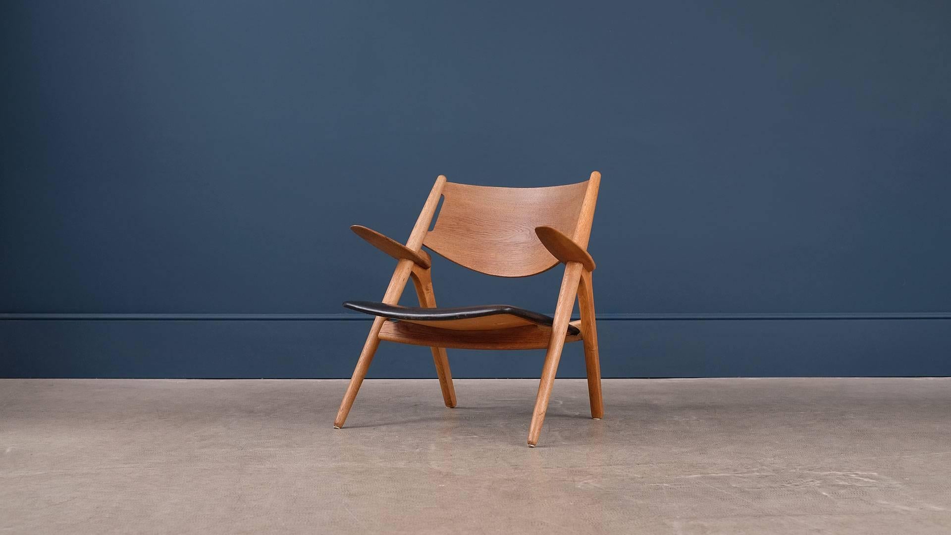 Beautiful CH28 or sawback lounge chair designed by Hans Wegner for Carl Hansen, Denmark. Early chair in oak with beautiful black leather seat and wonderful patina.