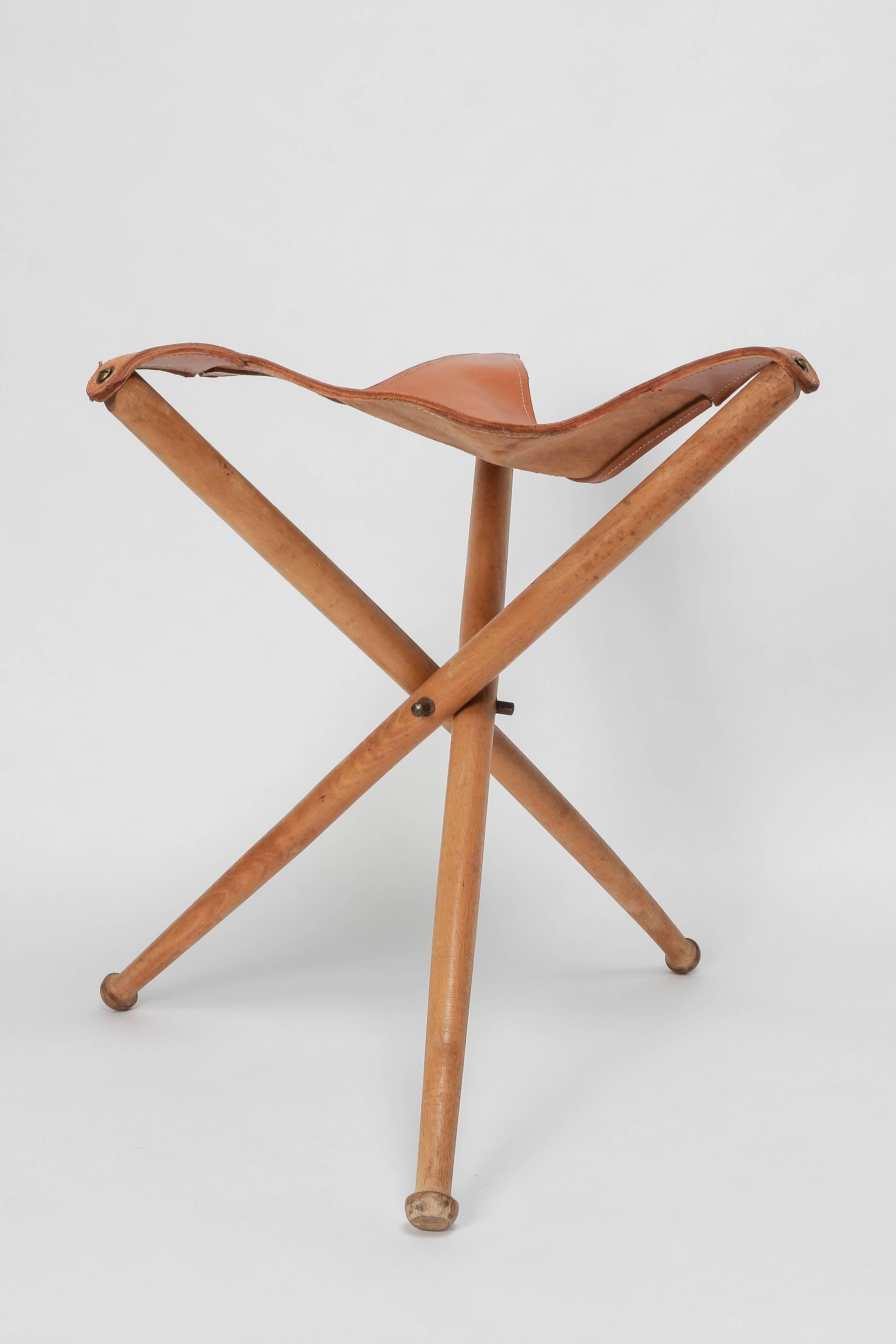 Tripod hunting stool with legs made of solid beech wood and a seat of thick saddle leather, manufactured in the 1940s. 65 cm long when folded.