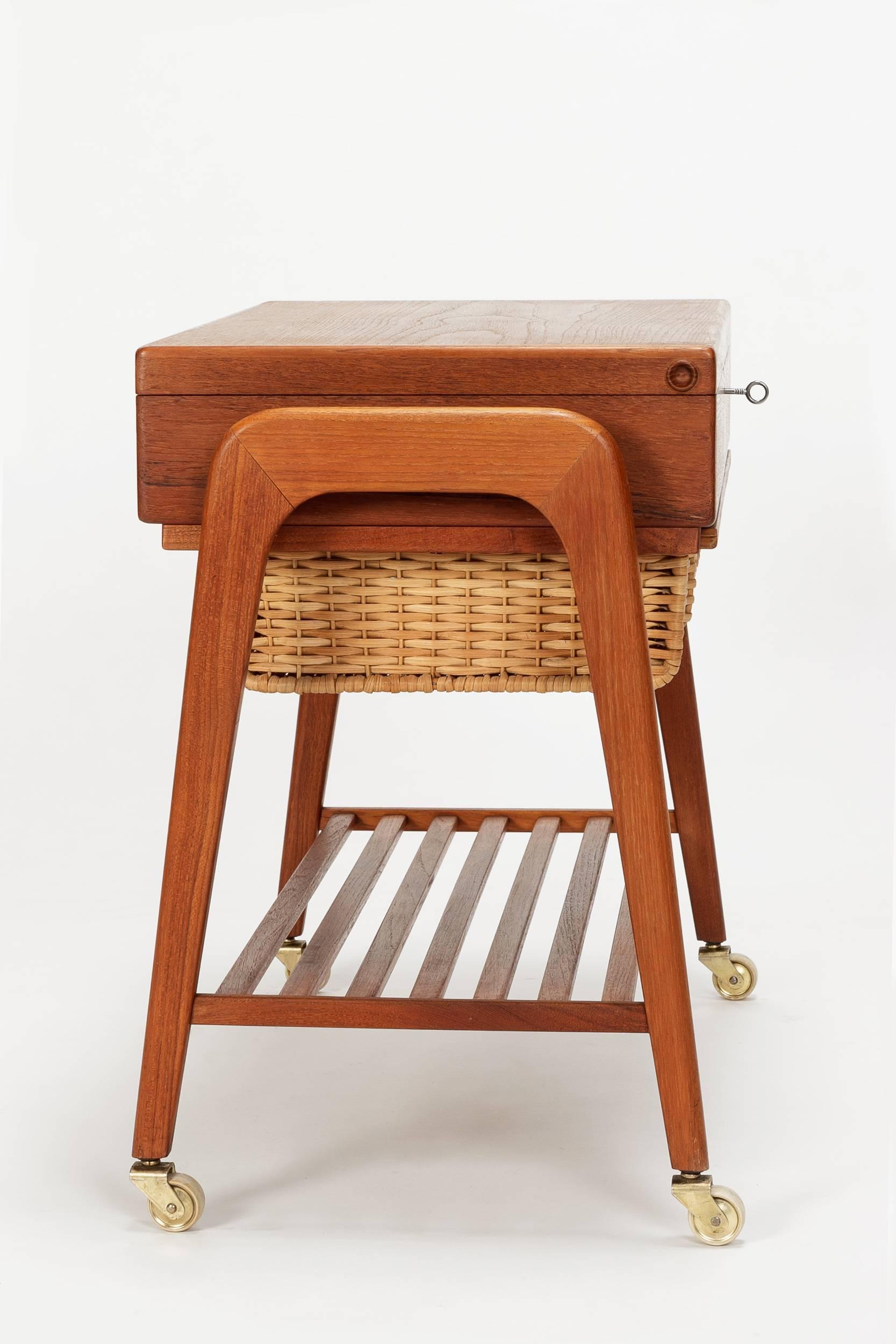 Danish modern sewing table designed by Povl Dinesen in the 1960s. Teak cabinet with locking drawer, a shelf and a sliding basket.