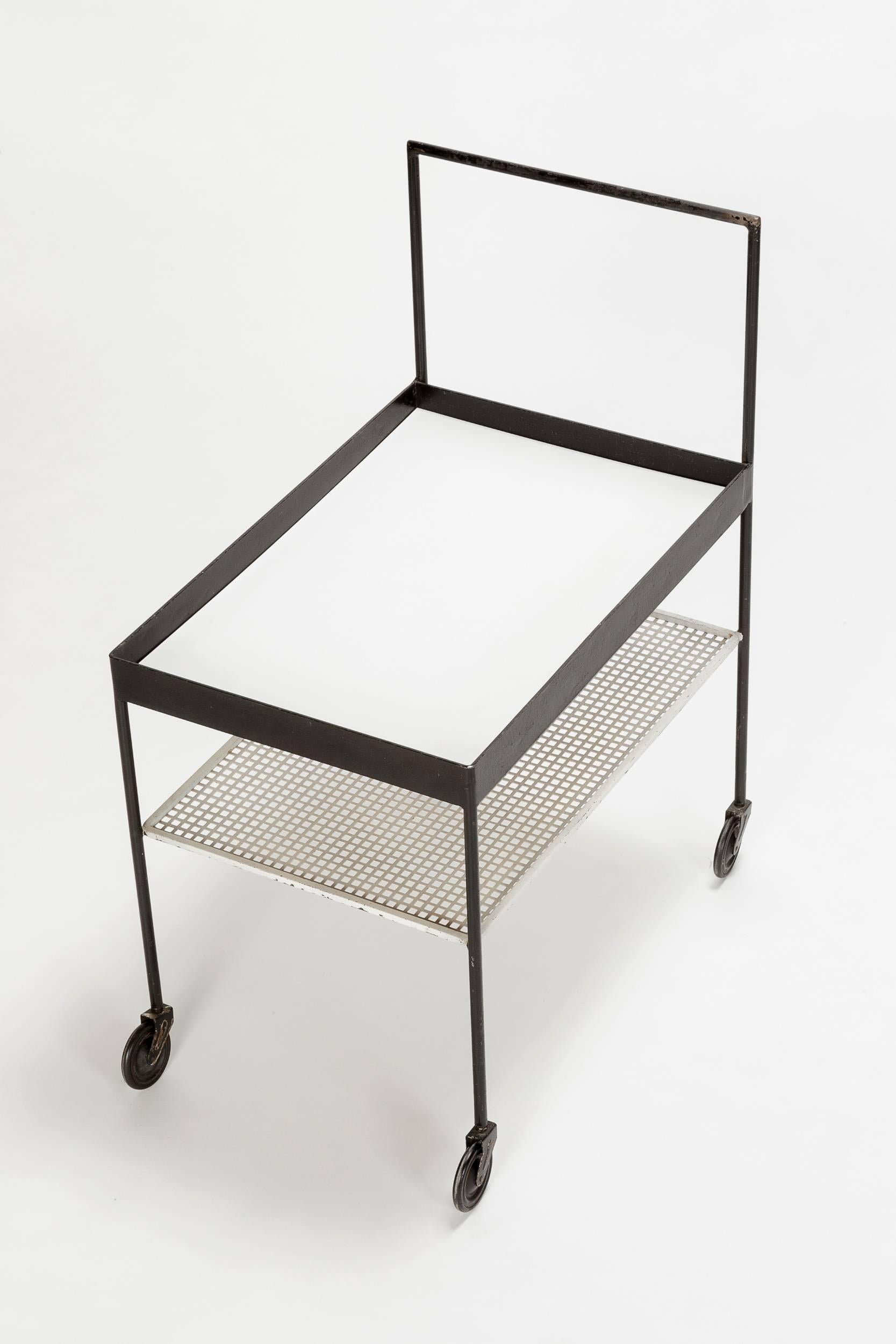 A wonderful geometric bar cart attributed to Mathieu Matégot in black and white lacquered metal, manufactured in France in the 1950s. Cut out white metal shelf space, the top is covered with white Formica. Original rubber coated wheels.