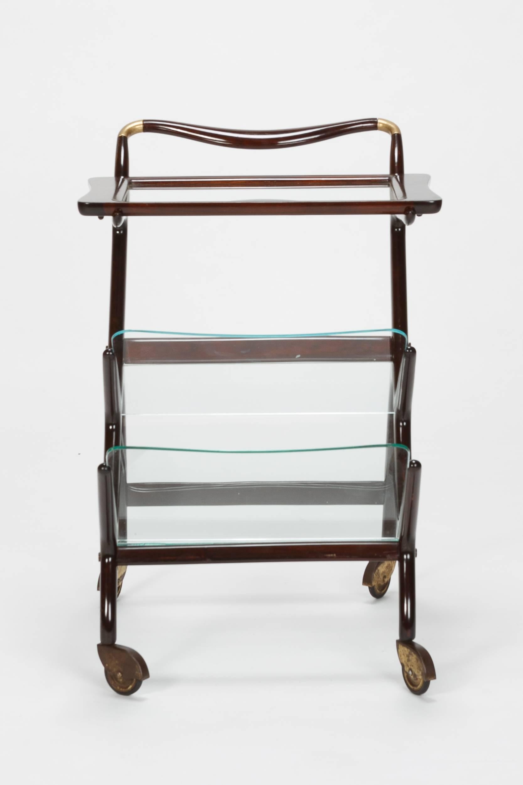 Wonderful Ico Parisi bar cart from the 1950s made of mahogany with original brass wheels. The top glass with wooden frame is removable and can be used as a tray. Two further glass shelves can be used as a newspaper rack. New lacquer.