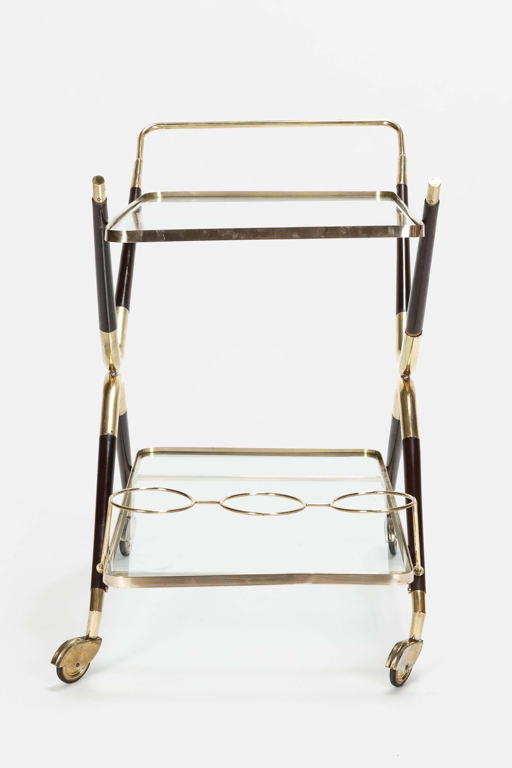 A stunning Cesare Lacca bar cart, manufactured in Italy in the 1950s. Very elegant and reduced shape with a frame of solid brass and shiny lacquered black mahogany, shelves made of original glass. Three bottle holder integrated on the lower shelf.