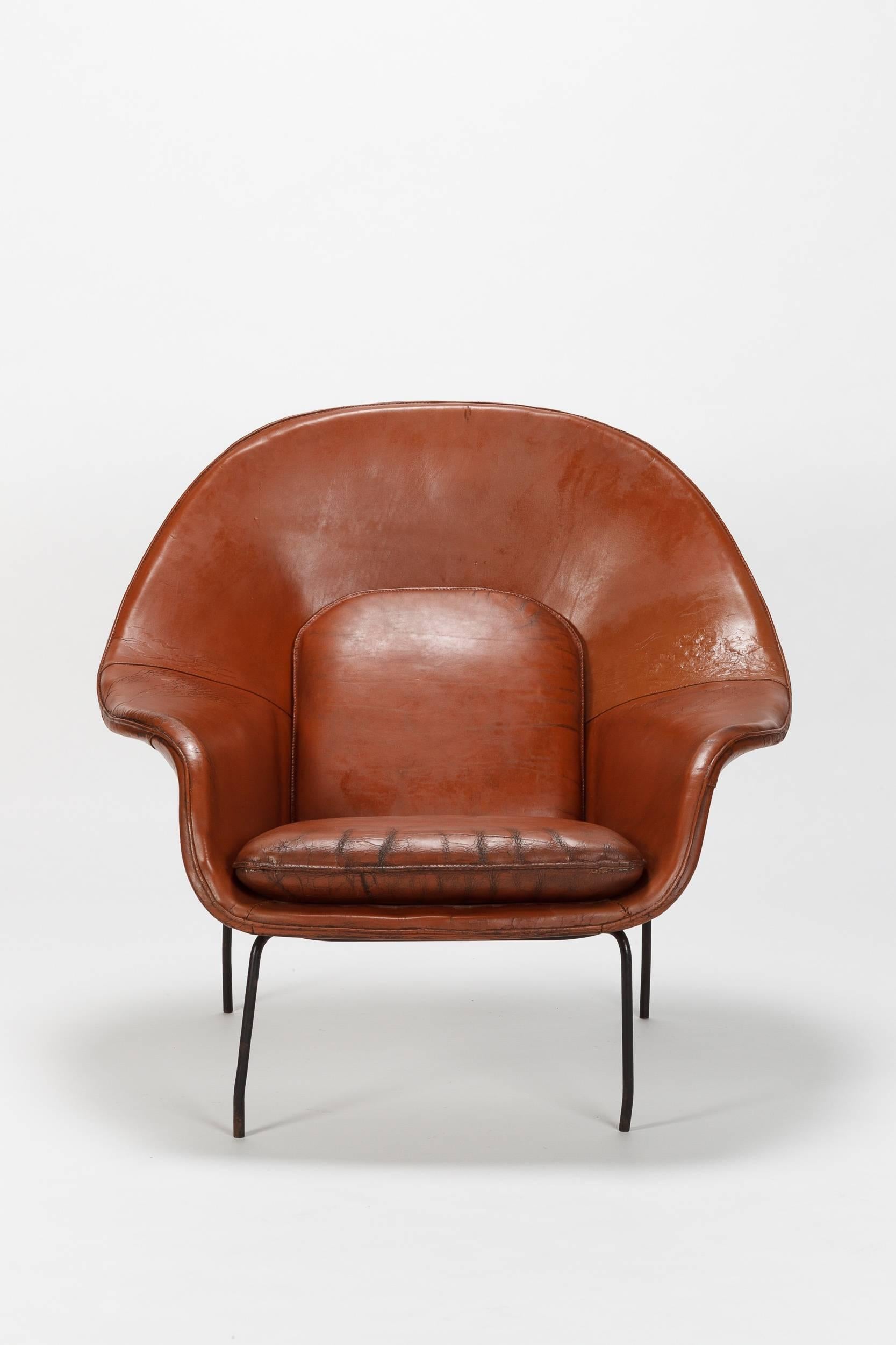 Eero Saarinen Womb chair designed 1948 and manufactured by Knoll. Beautiful brown leather and black metal base. Florence Knoll charged Eero Saarinen to design "a chair that was like a basket full of pillows, something I could really curl up