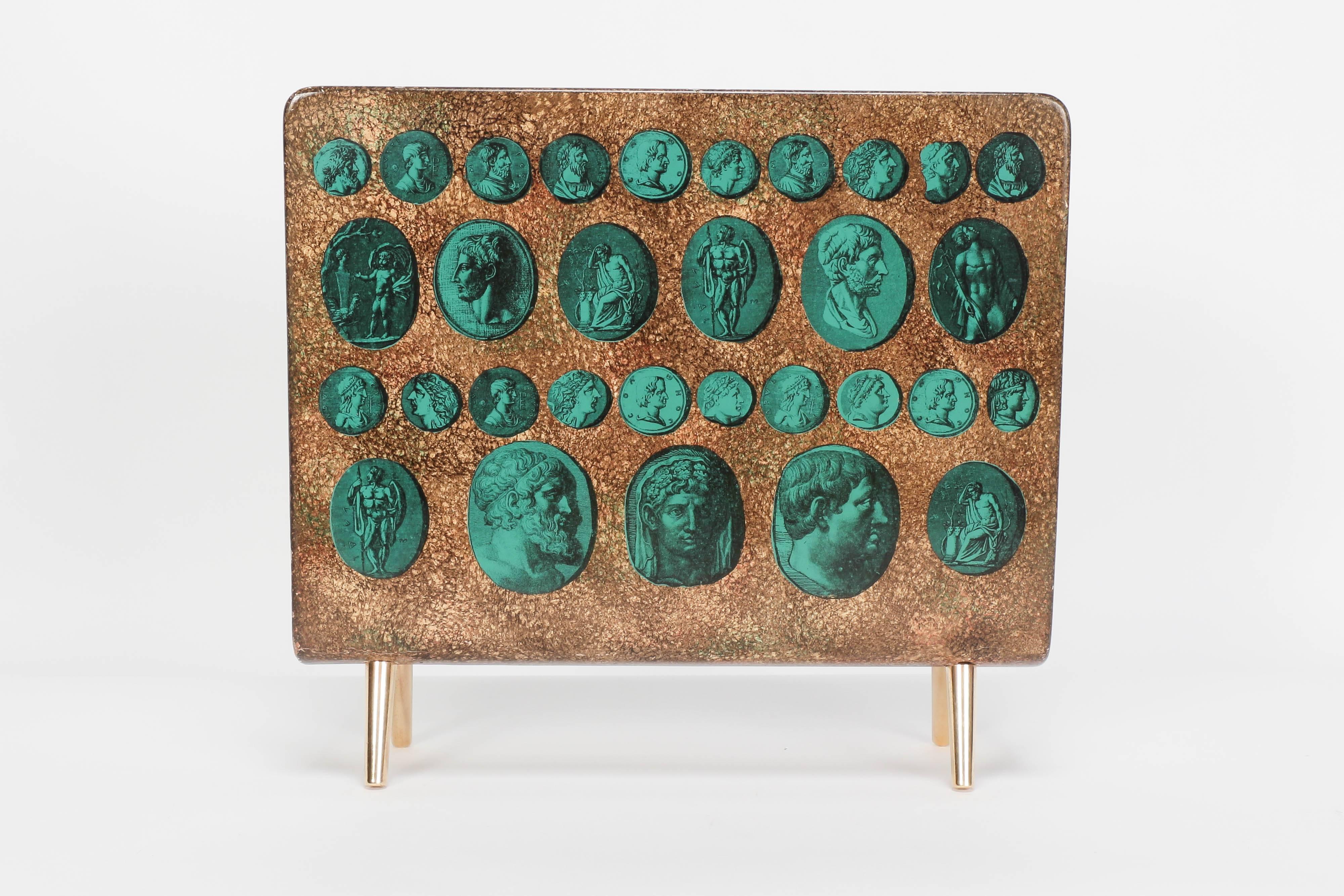 Handcrafted of lacquered wood embellished with a polished brass divider and feet. Fornasetti magazine rack painted with a pattern of antique coins.