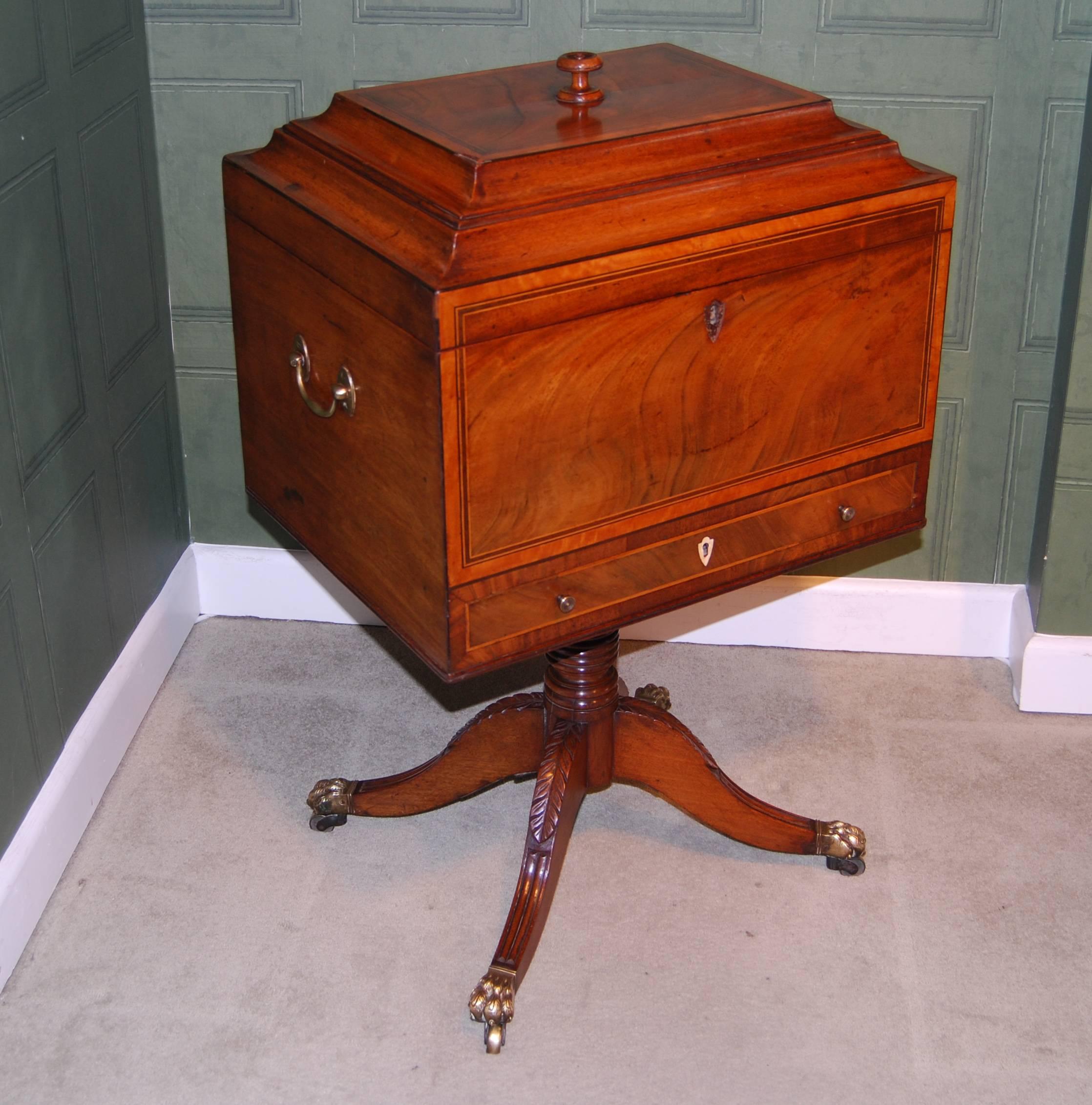 A Regency mahogany and satinwood teapoy or wine cooler with brass carrying handles to the sides, the hinged rectangular top with a central finial and opening to show a large reserve and two removable lidded compartments all above a drawer and the