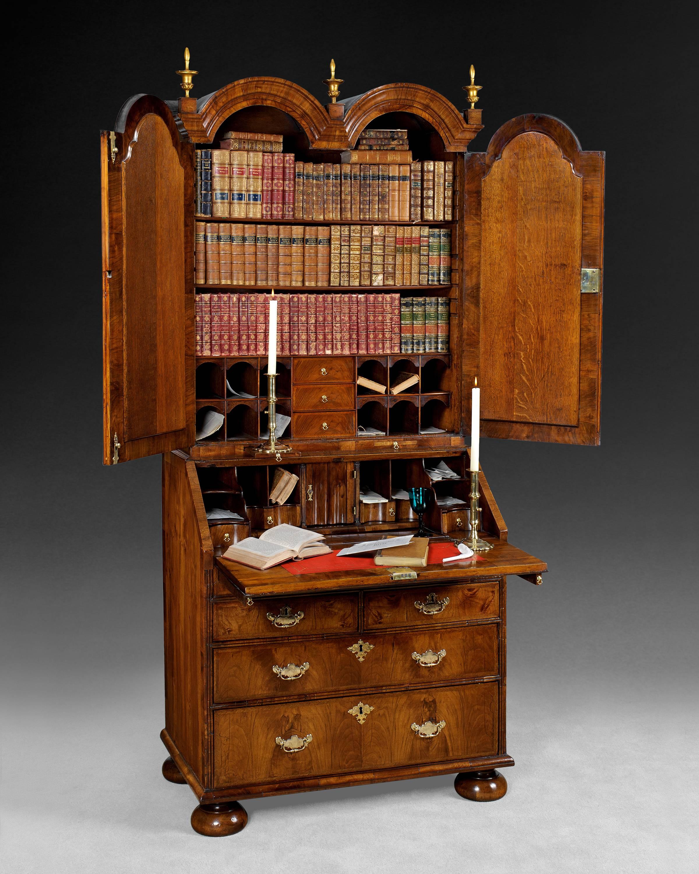 A fine and rare William and Mary period figured walnut double dome top bureau bookcase, the double domes with central and corner flanking carved giltwood finials and the crossbanded sides with domed returns at the top, the conforming doors to the