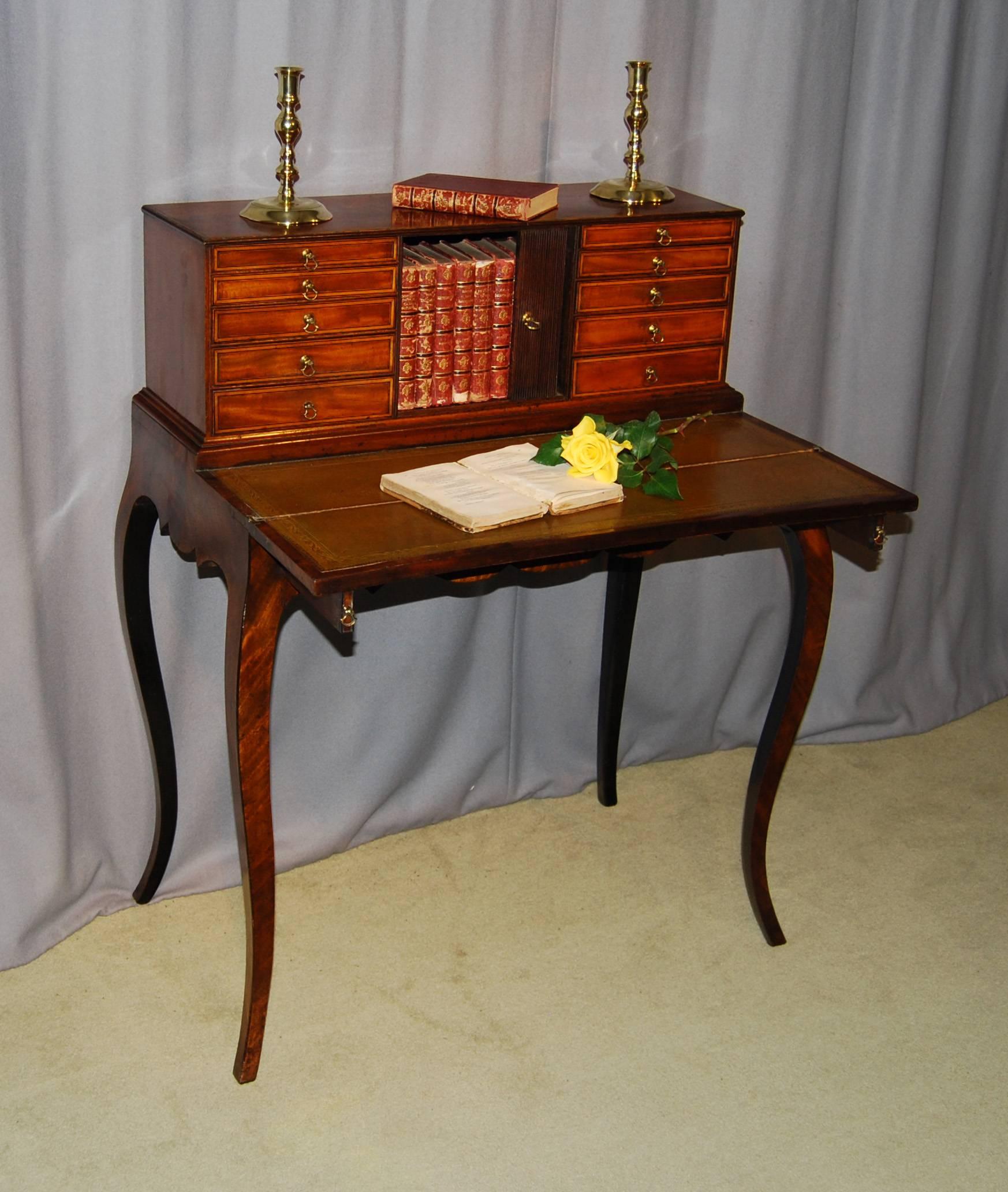 An exceptional George III period mahogany and inlaid Bonheur du Jour, the upper part fitted with two banks of five graduated drawers flanking a central tambour fronted cupboard all above a fold out leather lined writing flap supported by two