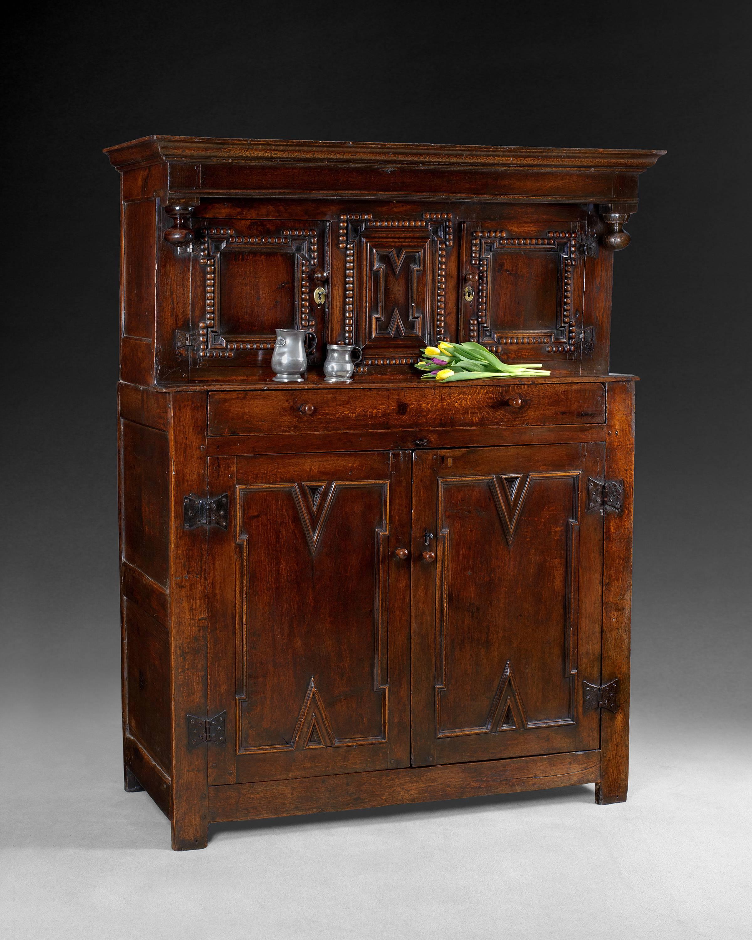 A good late 17th century carved oak court cupboard, the moulded canopy with drop finials, above a pair of geometric moulded cupboard doors with split bobbin turned borders, framing a conforming, central panel, set above an advanced lower section