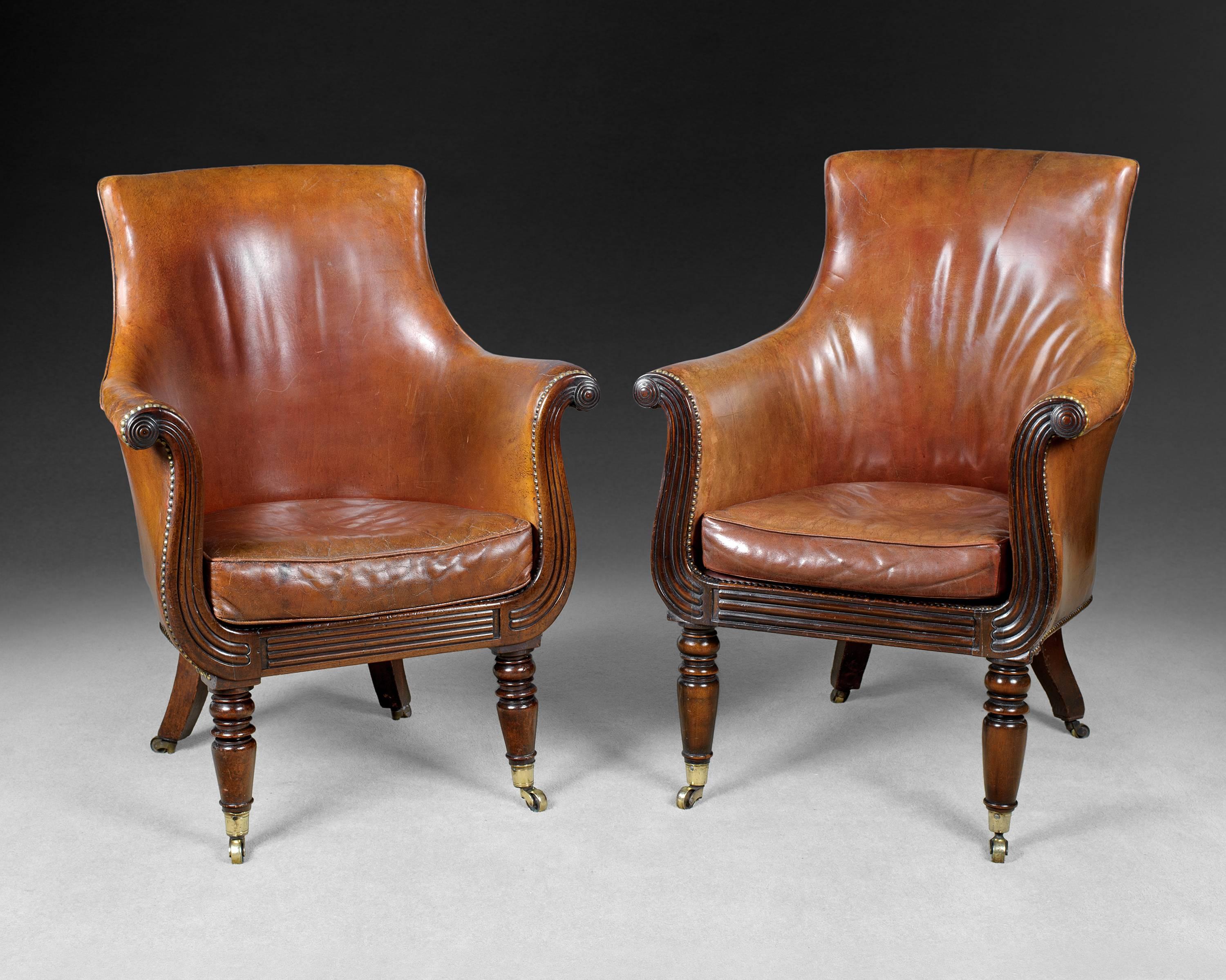A fine and rare pair of Regency mahogany library armchairs upholstered in faded red hide with brass nailing, the deeply shaped backs flanked by scrolling arms and raised on Lyre-shaped mahogany frames with reeded details and turned front legs