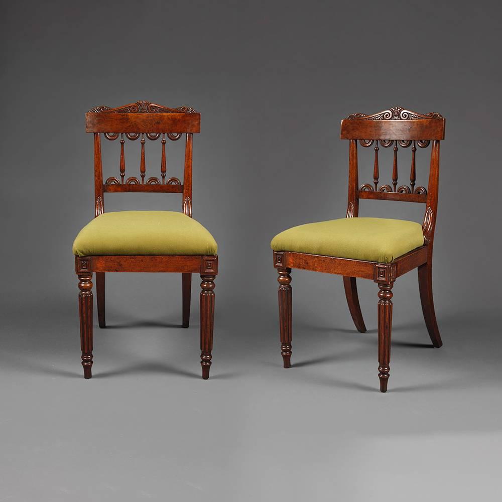 A pair of William IV burr oak side chairs with shaped and carved top rail over pierced back support over stuffed seat on reeded and columned legs.