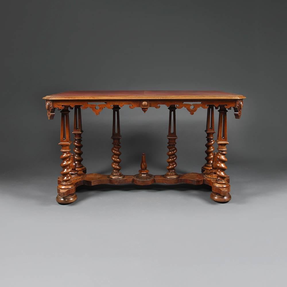 A late 19th century walnut Gothic writing desk attributed to Richard Bridgens with tooled red leather top over pierced and shaped frieze on six tapered can columned legs with barley twist supports on shaped and mounted stretcher terminating in bun