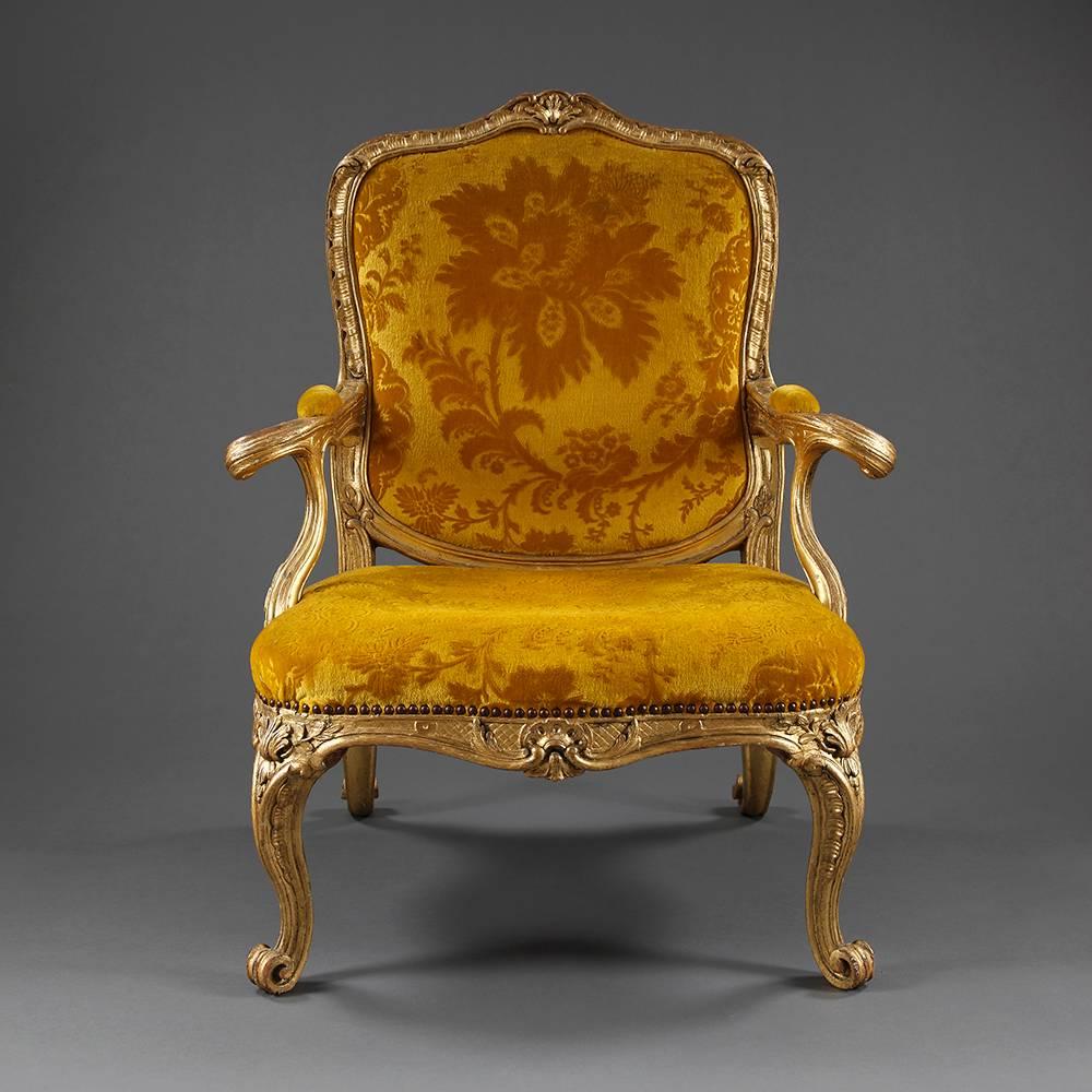 Each with cartouche-shaped back, armrests and seat covered in yellow cut velvet, the foliate-carved channeled frame without scrolled arms and rocaille-carved serpentine seat, on cabriole legs and scroll feet, re-gilt, both with pegged construction