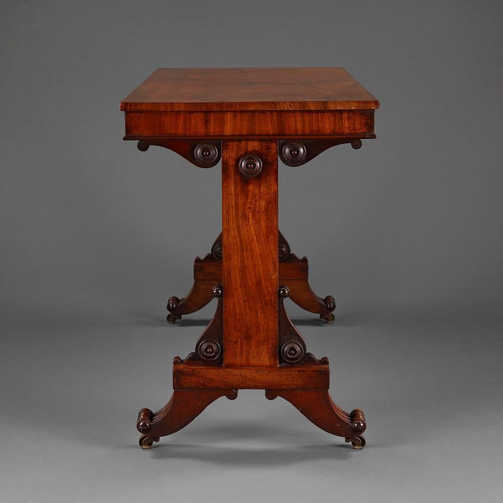 A William IV period flame mahogany writing desk with plain top over veneered frieze on two vertical supports each decorated with turned and moulded roundels on squared bases above splayed feet mounted on original castors. The whole of good faded