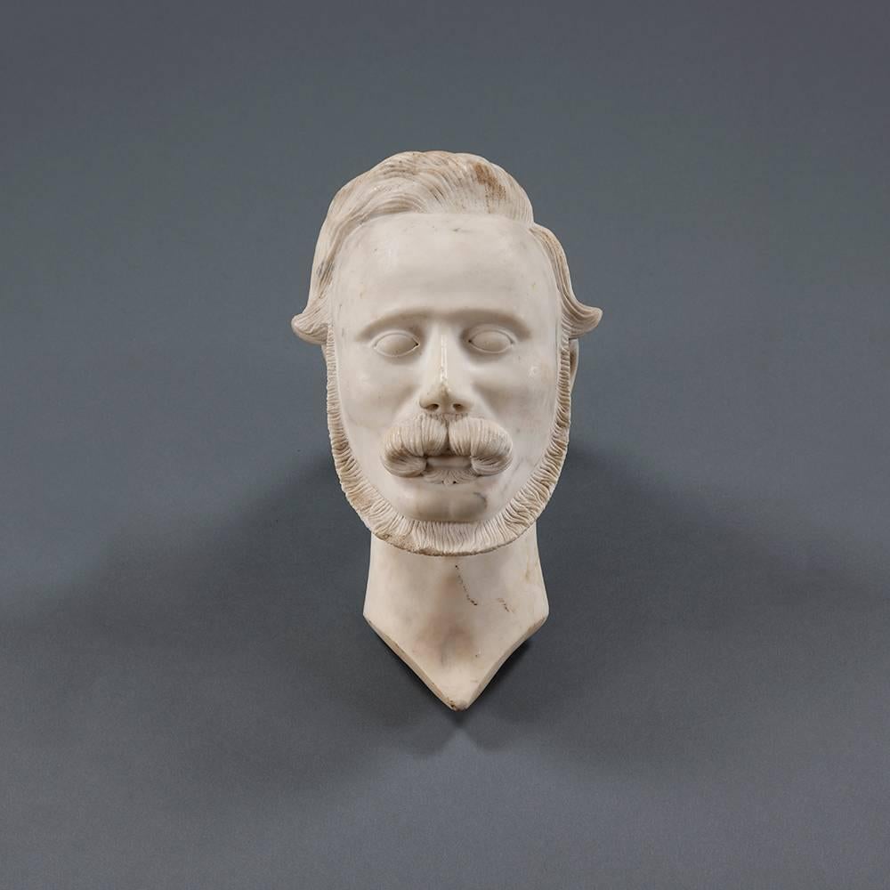 A mid-19th century detailed carving of a mans head with off set side parting and a pointed nose above moustache and beard.