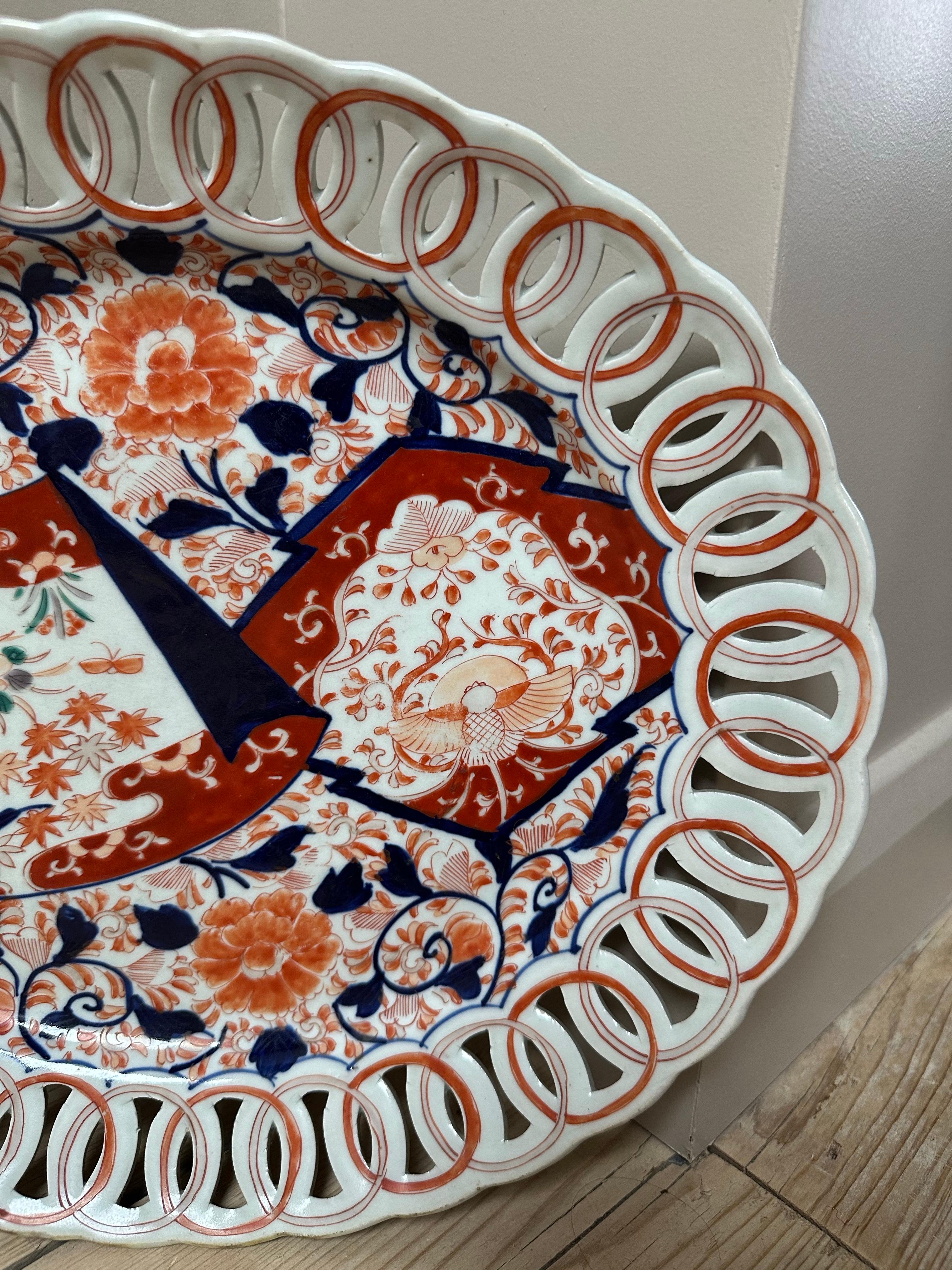Il s'agit d'une assiette Imari, caractérisée par ses couleurs vibrantes et ses motifs complexes. Il présente un bord percé en forme d'anneau, un trait commun à la céramique Imari, qui lui confère un attrait décoratif distinctif. L'assiette est ornée
