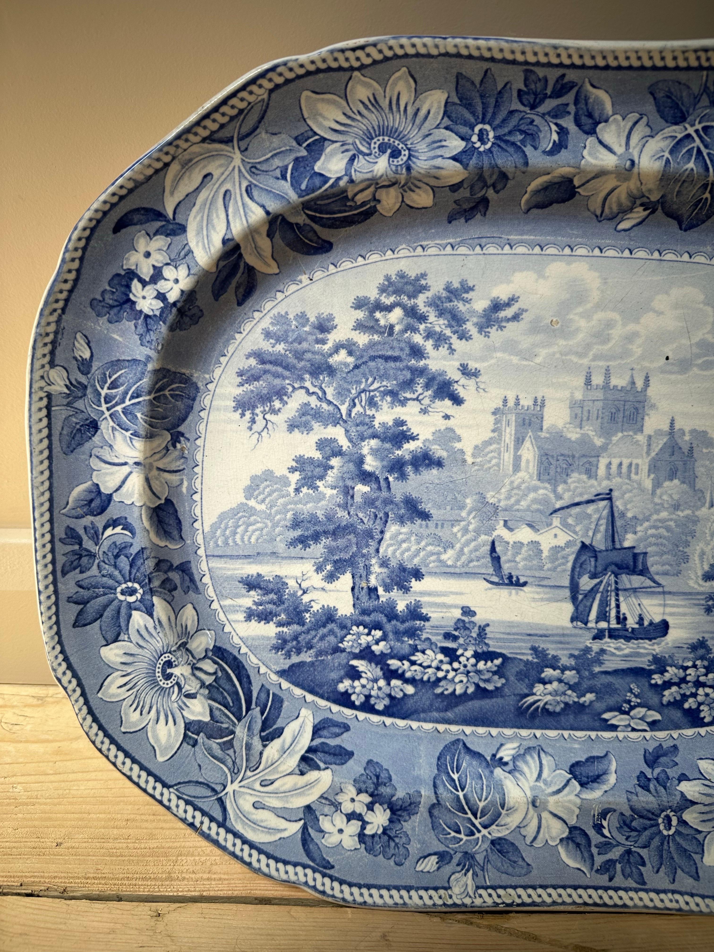 L'image montre un plat ancien en transferware bleu et blanc du Staffordshire, datant du début du 19e siècle. Ce plat spécifique présente le motif 