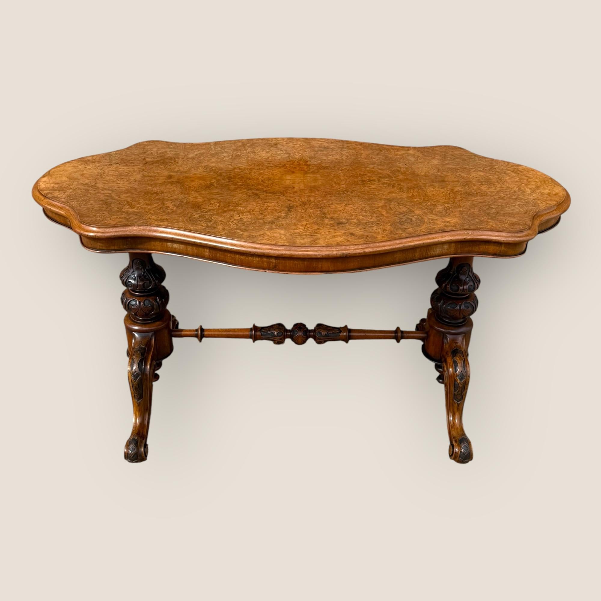 Here we have a Victorian (1837-1901) Burr Walnut Centre Table. The serpentine shaped top is quarter veneered with burr walnut and it stands on turned stretcher legs with detailed carved columns and finials to the underside of each arch.