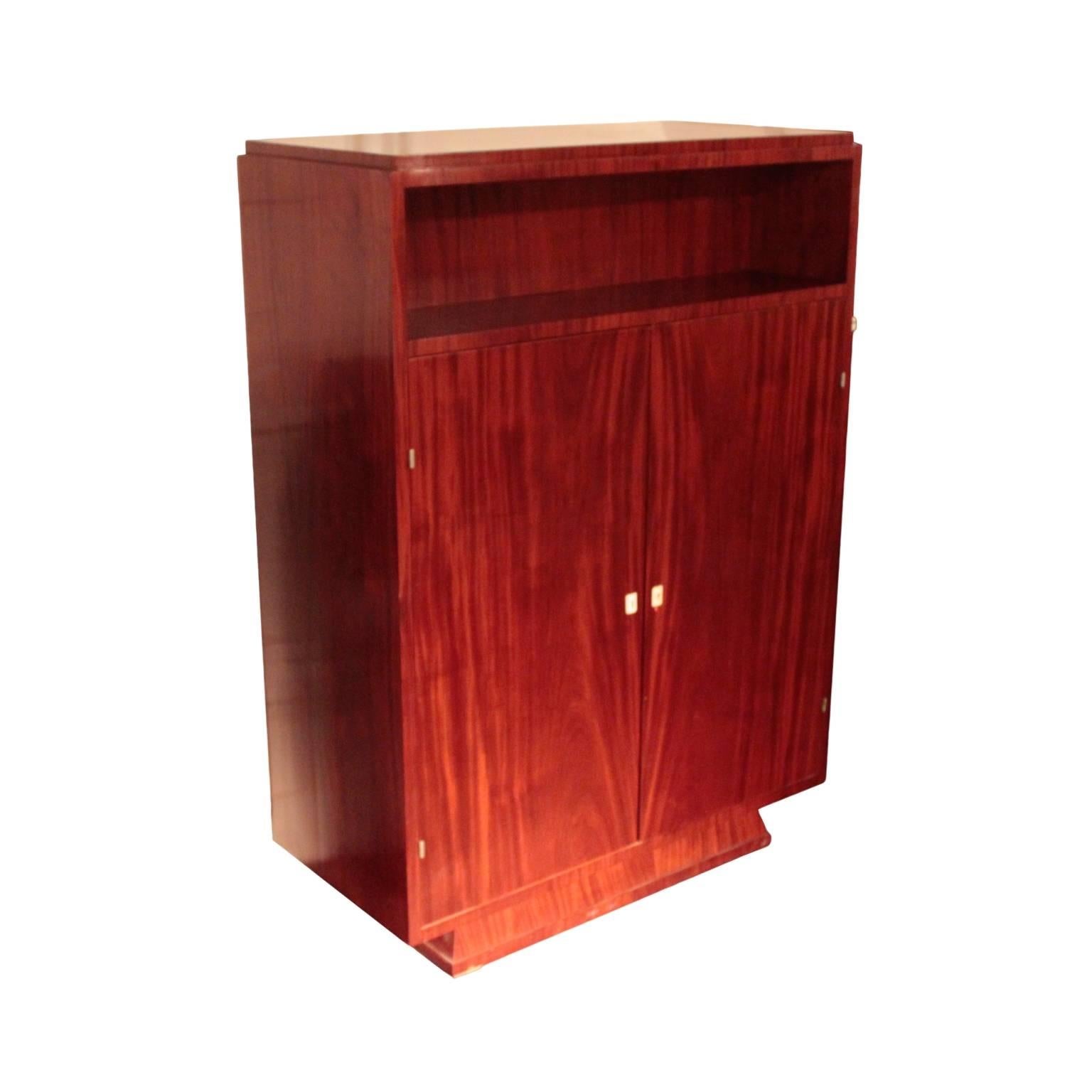 French Art Deco period cabinet of excellent quality in the manner of Jules Leleu, in solid and veneered African ribbon mahogany, including interior. Cuboid shaped body having an exposed niche on top of a pair of doors fitted with ivory escutcheons