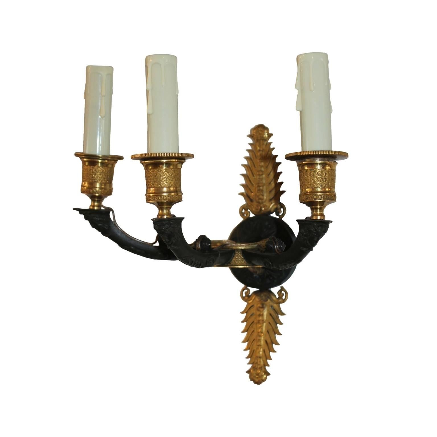 Dark verde antico bronze sconces with bronze doré anthemion ormolus. Each with three arms decorated with an acanthus leaf and a face of a young Frenchman with aquline nose, long curls and a neckerchief (depiction of young Bonaparte?) supporting