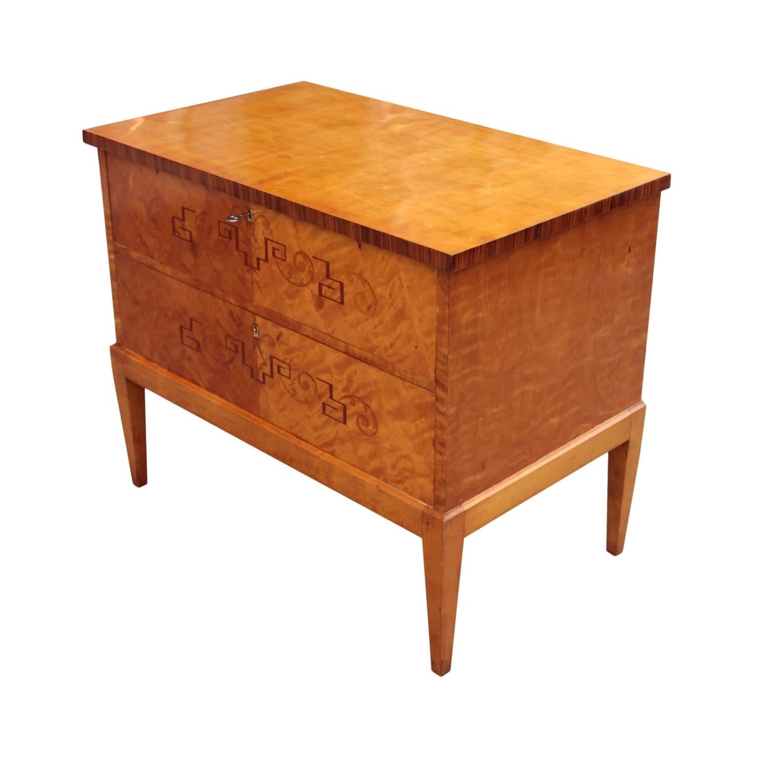 Elegant Swedish neoclassical small chest made during Grace period (1920's). Protruding top with rosewood edge resting on a cabinet with two drawers decorated with inlays in rosewood, walnut and maple depicting acanthus leaves and meanders. Raised on