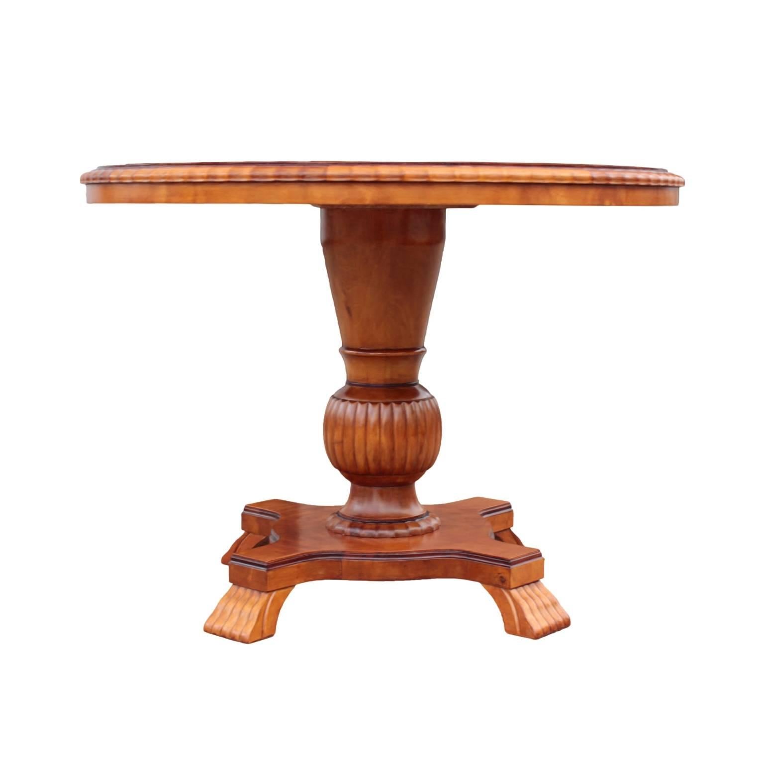 Round stepped table top with scalloped edge in bookmatched flame birch raised on reeded urn pedestal with scalloped plinth, the whole resting on a quadripartite base with stylized paw feet. In flame birch with dark accents.