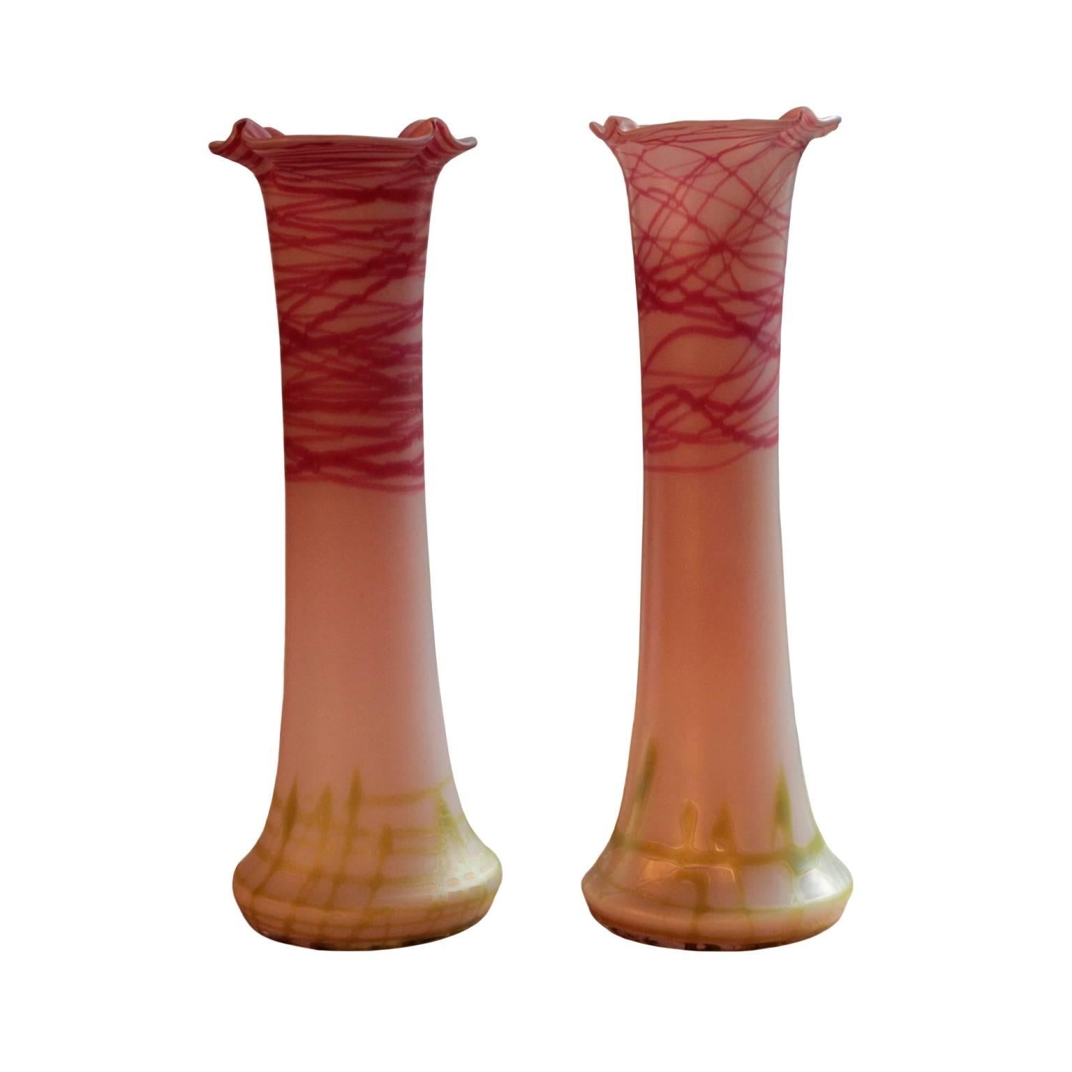 Slim and narrow bodies in colorless glass with wide pinched mouths featuring molded rims; decorated with beautiful raspberry red and light green liberally applied horizontal and vertical patterns. Made by Glasfabrik Elisabeth (or Pallme-Koenig),