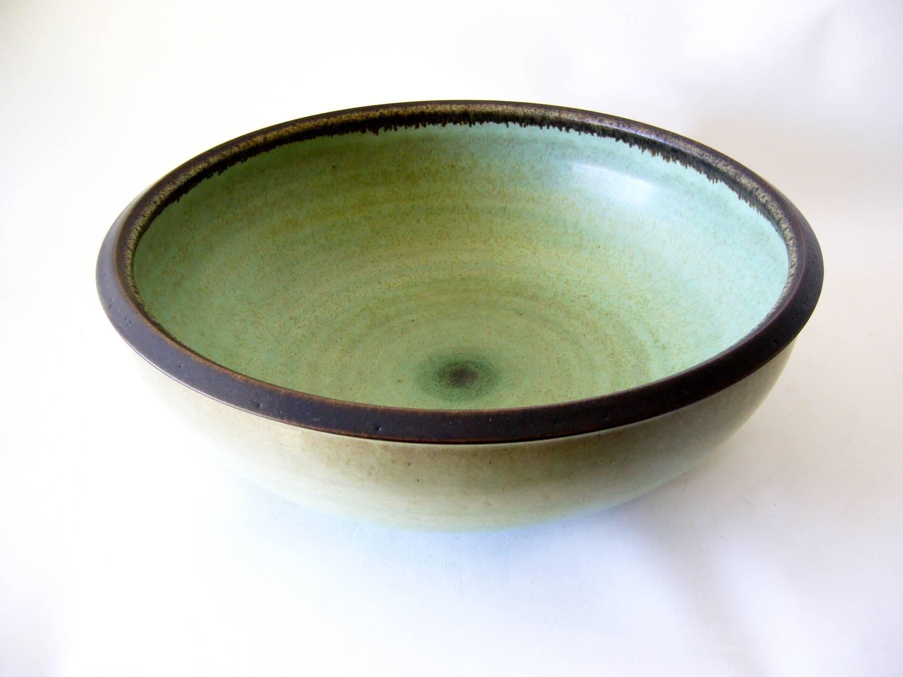 Large celedon glazed open stoneware bowl created by master ceramist Harrison McIntosh of Claremont, California. Great color combination of variations in celadon green on the interior, low lighted with a dark brown matte glazed rim. Piece measures