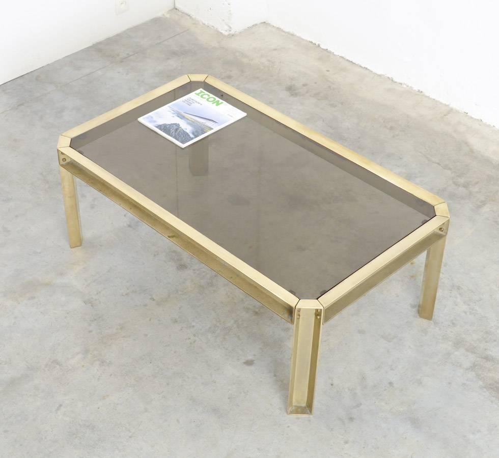 This solid brass coffee table is a nice example of luxury 1970s design. The sand cast brass feet are visible fixed with screws. The top is made of smoked glass. It is a pure and solid coffee table in good vintage condition, with normal signs of age
