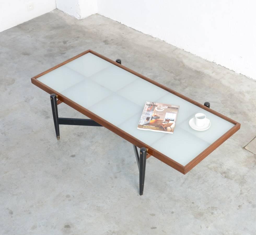 This coffee table of the 1950s is really a unique piece.
It is a beautiful design and perfectly made: The elegant black lacquered base with brass details, the lattice construction in natural teakwood and the opal glass top.
It could be a design of