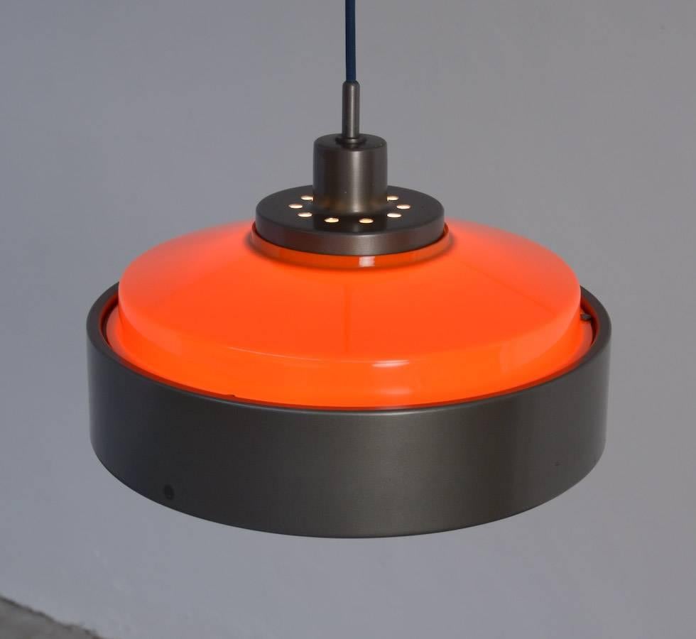 Gino Sarfatti designed in 1958 the 2098 pendant lamp for Arteluce.
This lamp is made of dark grey lacquered aluminium, as well as the ceiling cup.
Both shades are made of perspex: the under shade in white perspex and the upper shade in orange