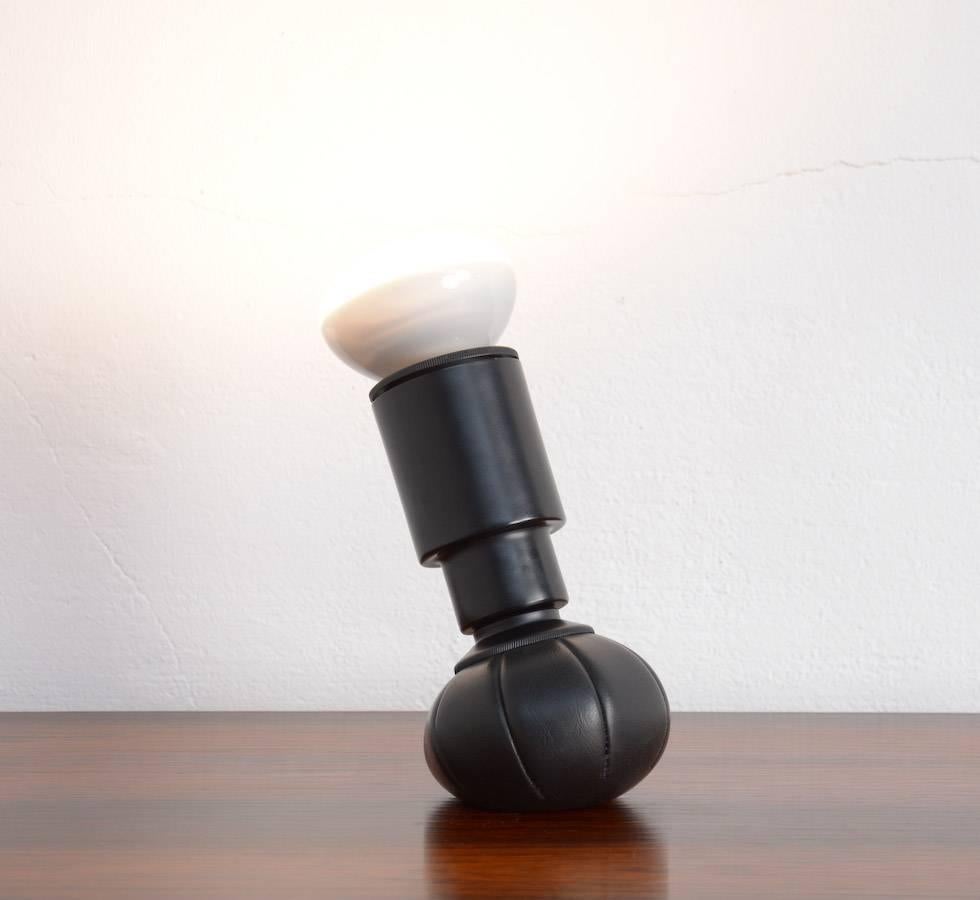 This old original table lamp 600g was designed by Gino Sarfatti for Arteluce in 1966.
This lamp is made of black lacquered aluminum and it has a support of a pouch made of black sky leather, filled with lead shot.
This type of support allows the