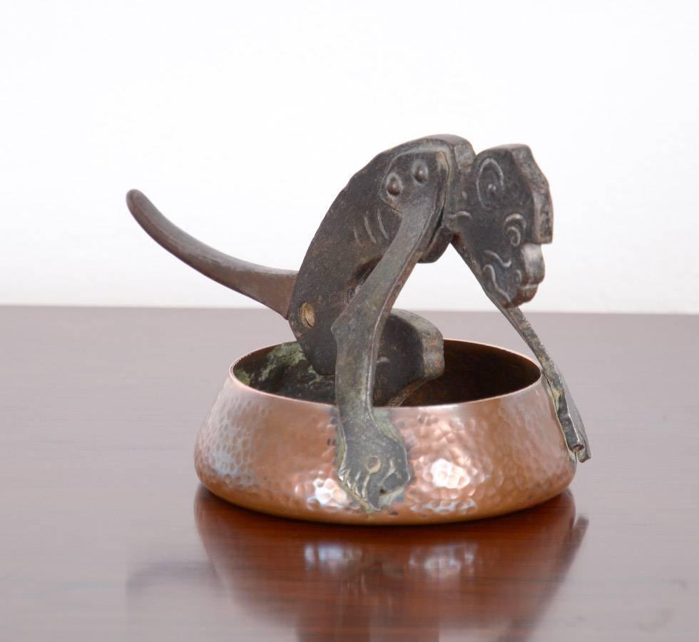 This cigar cutter was designed by the German artist Ignatius Taschner, Germany, circa 1905.
You can cut the cigar with the monkey’s tail. The cigar tip will fall into the copper bin.
The monkey is made of steel and has a black finish, the bin is