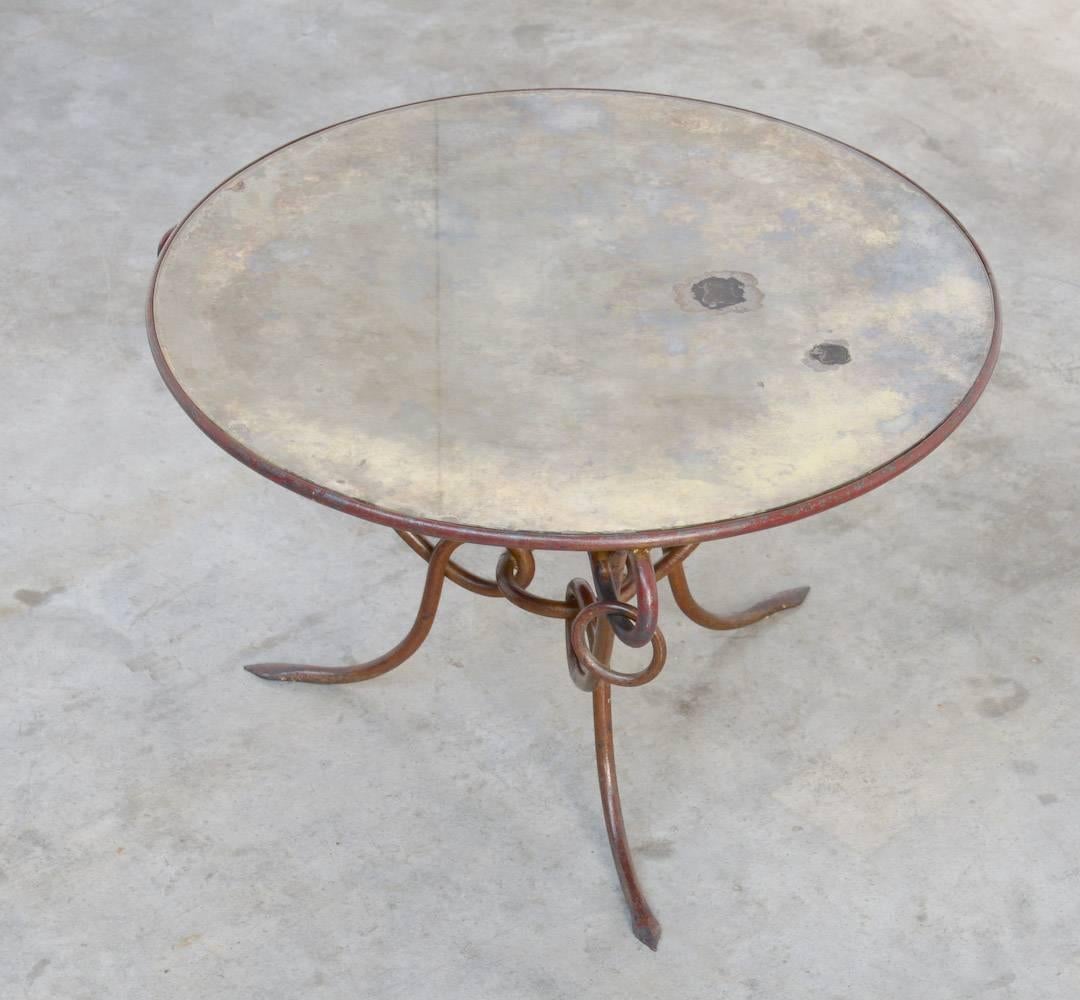 This round forged gilded iron coffee table was designed by René Drouet (1899–1993) in the 1940s. The base is made of forged iron with its original dark red and gilded gold patina. The original top in silvered ‘mirrored’ glass has some spots due to