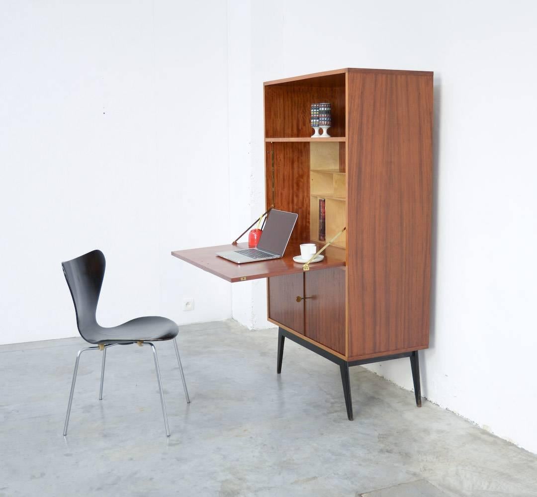 This writing cabinet was designed by Alfred Hendrickx for Belform in the late 1950s.
The nice wood pattern, the details in light wood, the elegant black lacquered feet and the Fine copper handles make it an elegant piece of furniture. This cabinet