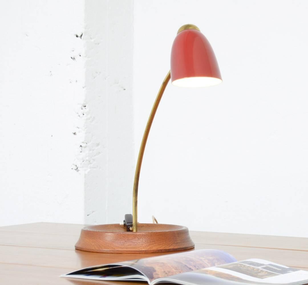 This unique table lamp is an Italian design of the 1950s.
It is probably produced by Arredoluce.
The teak wooden base holds the brass stem. The dark red lacquered metal shade has a nice brass detail. It reminds at the early work of Sottsass for